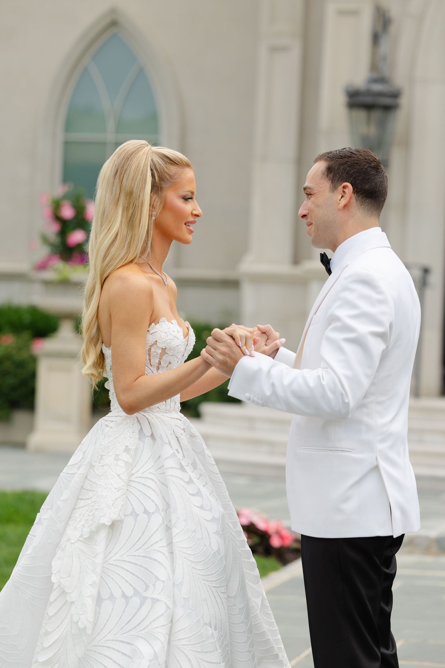 A bride and groom dance together on their wedding day in front of a white stone building with arched windows.