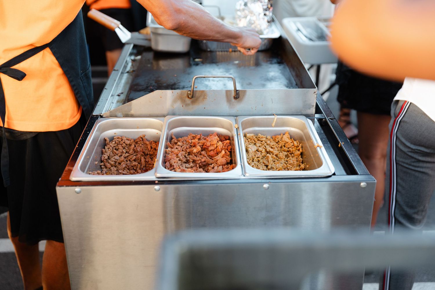 Three stainless steel food warmers containing different meat dishes in a buffet service line.