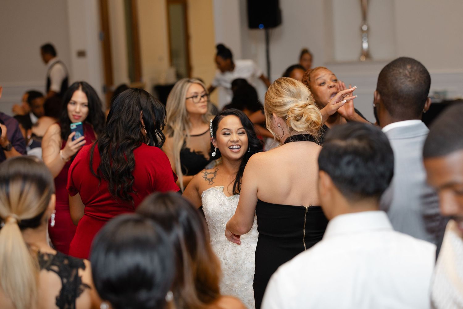 A lively wedding reception shows guests dancing and socializing in a bright indoor venue.