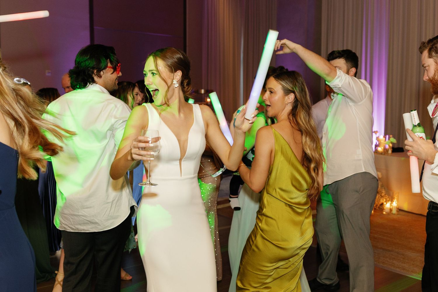Wedding guests dancing and celebrating on a dance floor illuminated by colorful party lights.