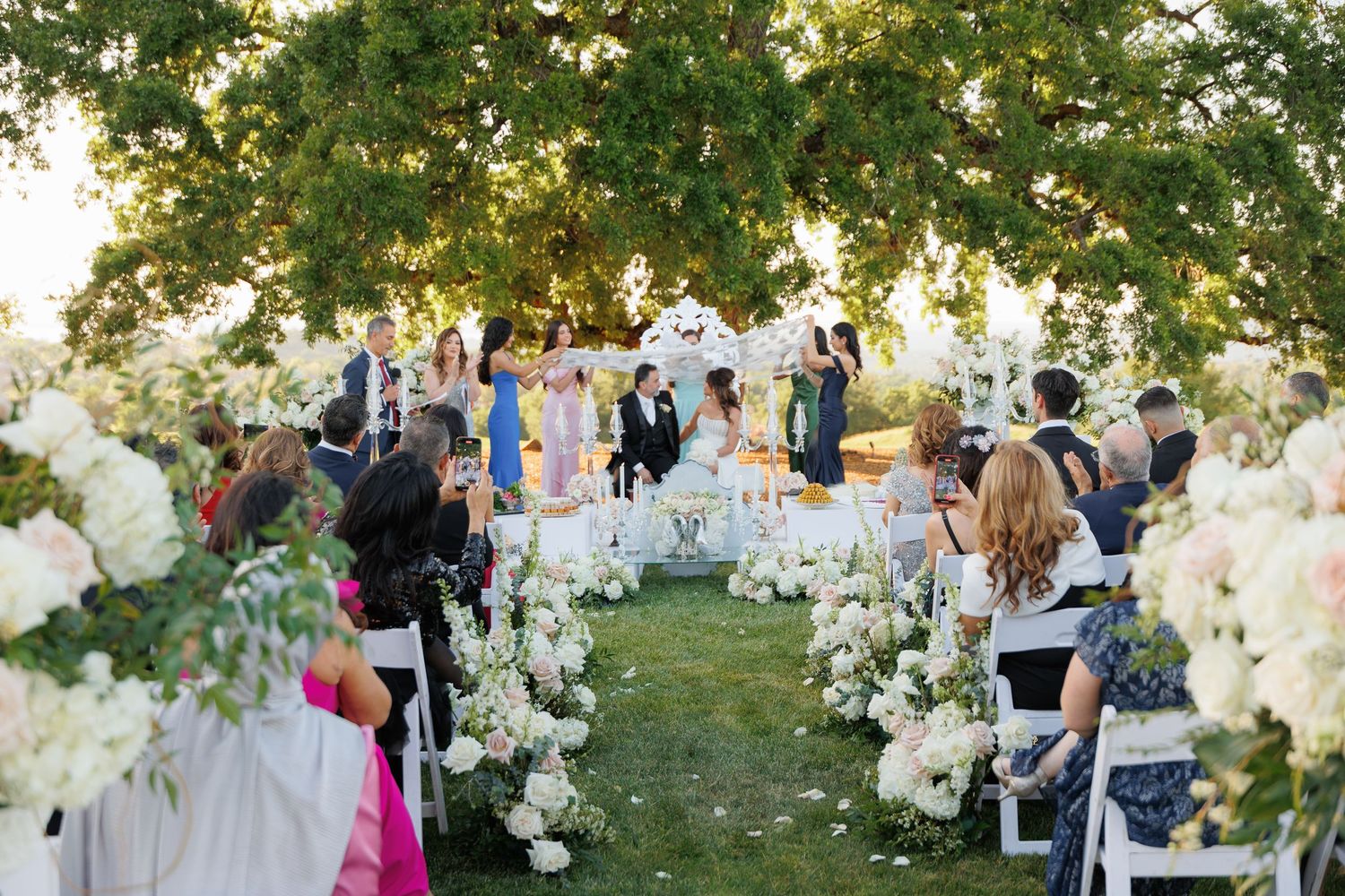 Guests mingle and socialize during an elegant outdoor garden wedding reception with white floral decorations.
