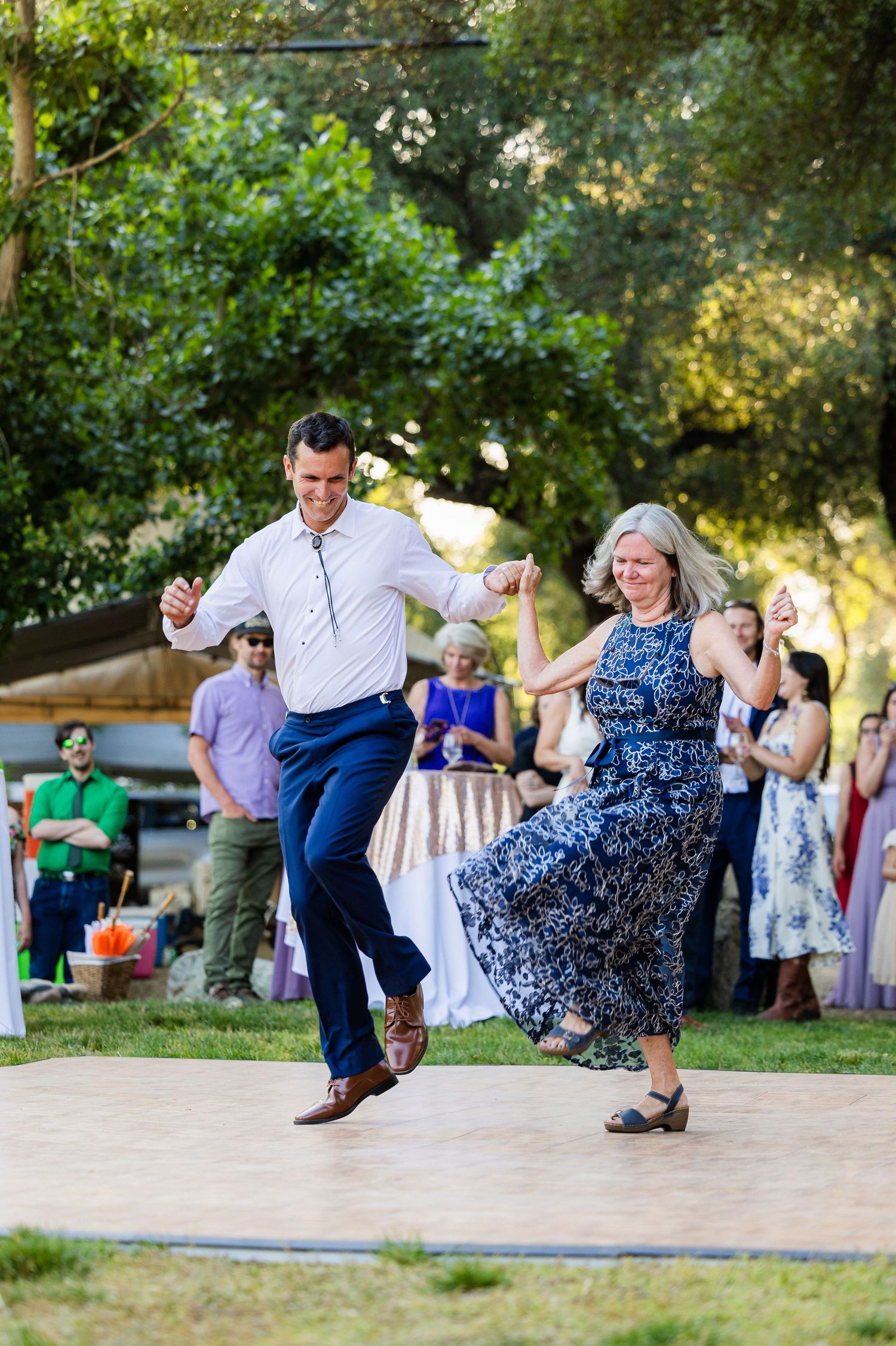 A couple performs an energetic swing dance move outdoors in a park setting during a summer event.