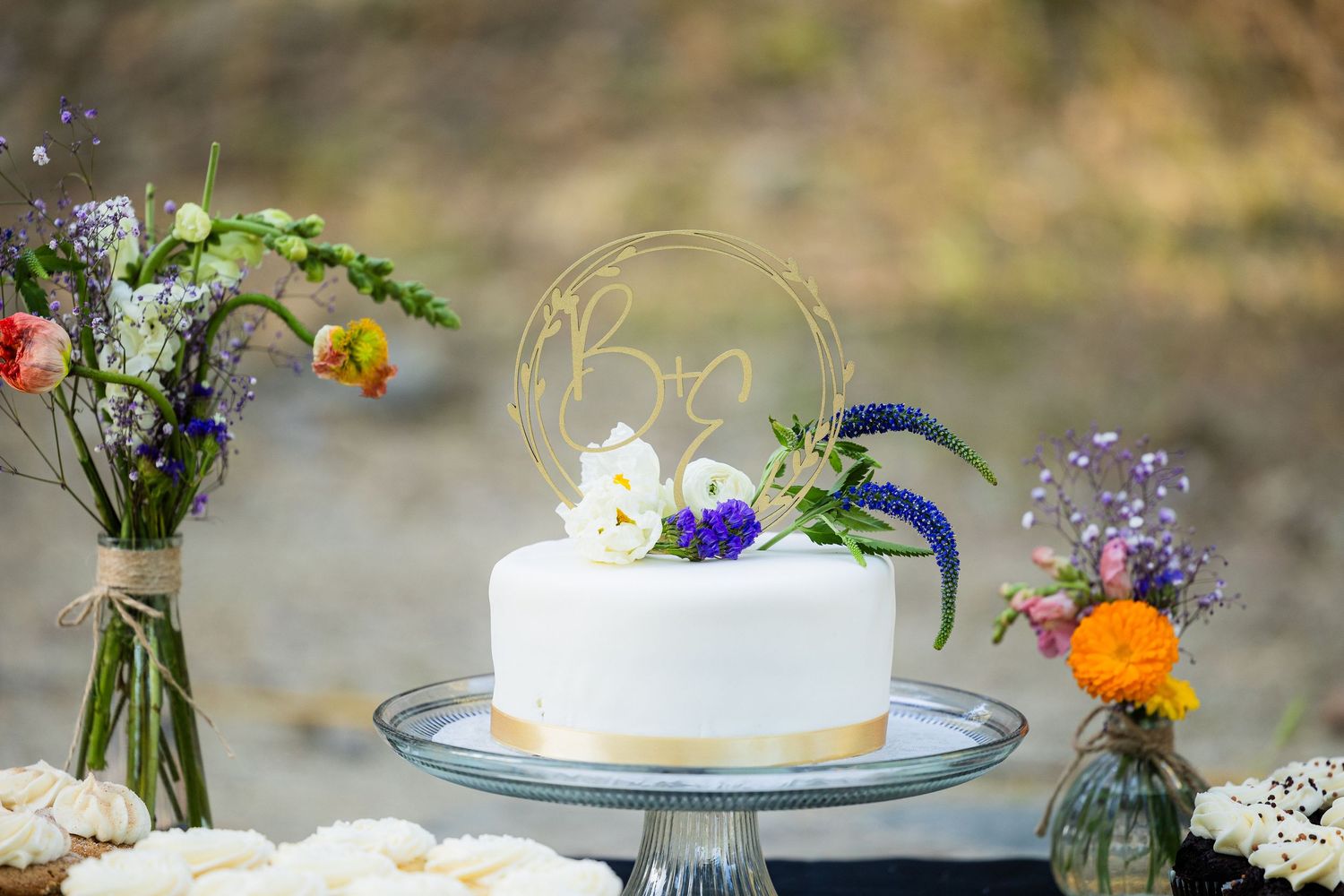 A collection of elegant white wedding cakes decorated with fresh flowers and greenery on rustic wooden tables.