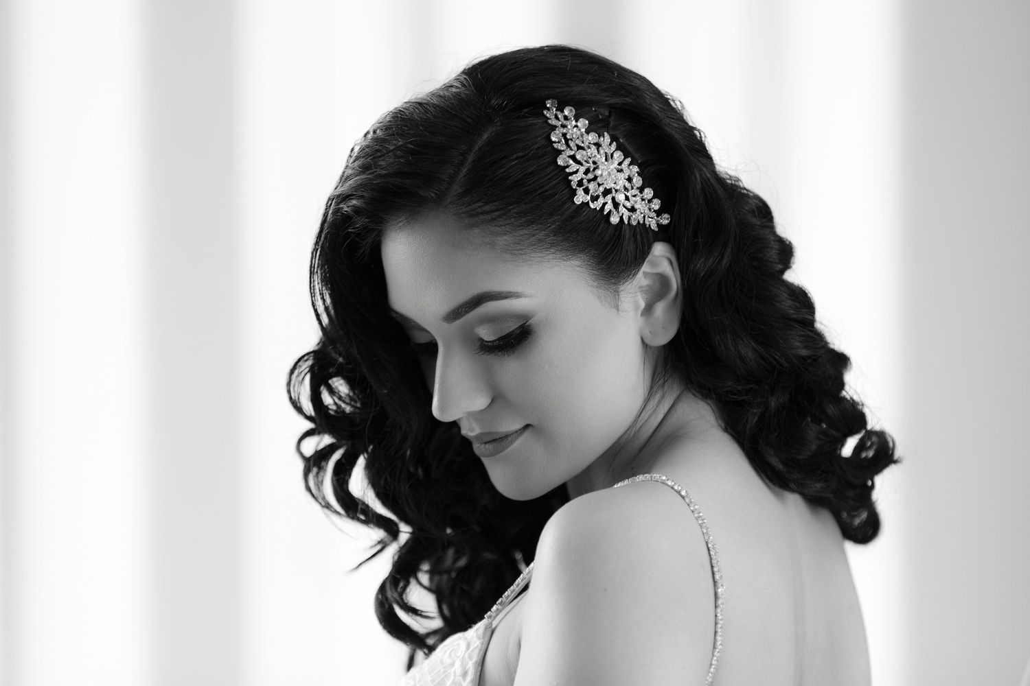 A bride in a white dress and crystal headpiece poses in an elegant black and white portrait.