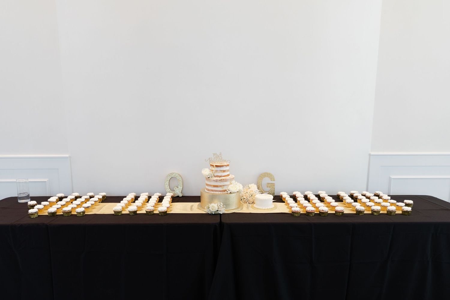 A minimalist table setup with wooden place settings and centerpieces arranged on a black tablecloth against a white wall.