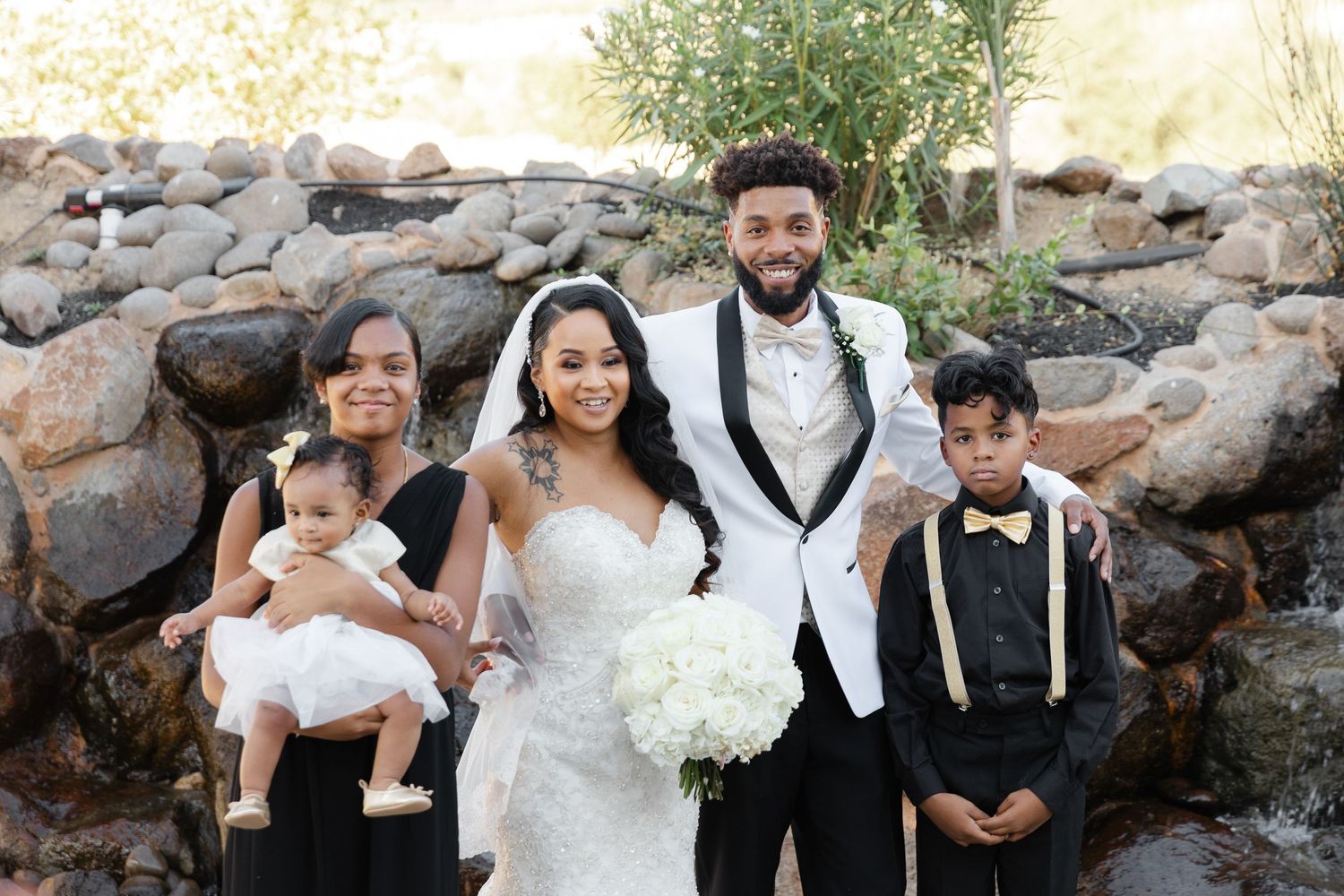 Wedding party poses outdoors against a rustic stone wall backdrop during a joyful celebration.