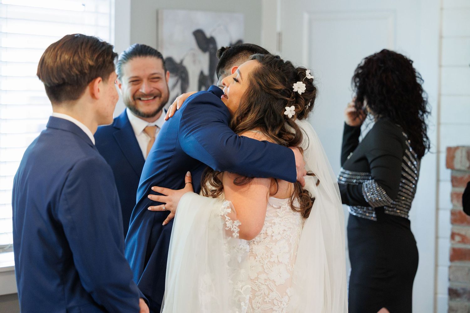 Wedding guests embrace and dance together during a joyful reception celebration in a bright indoor venue.