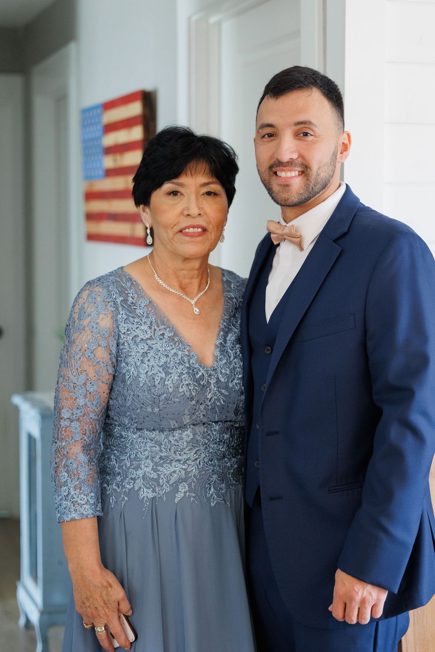 A woman in a grey lace evening gown poses with a man wearing a navy suit at a formal event.