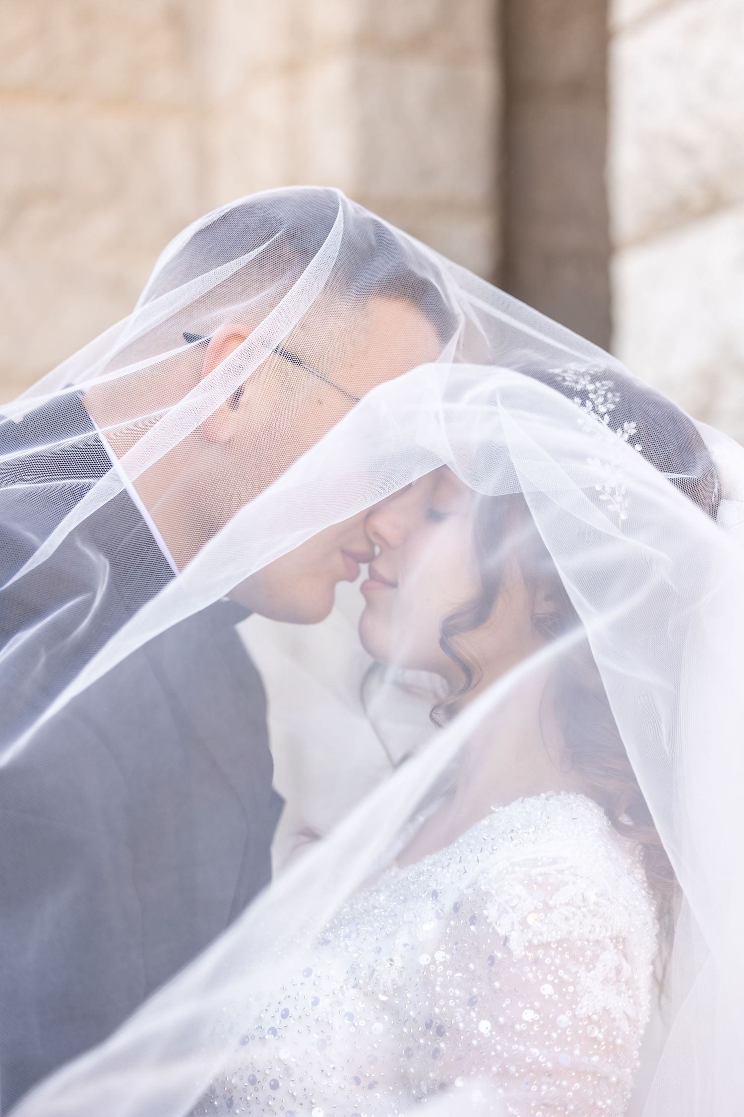 Romantic couple shares tender moment under flowing white wedding veil.