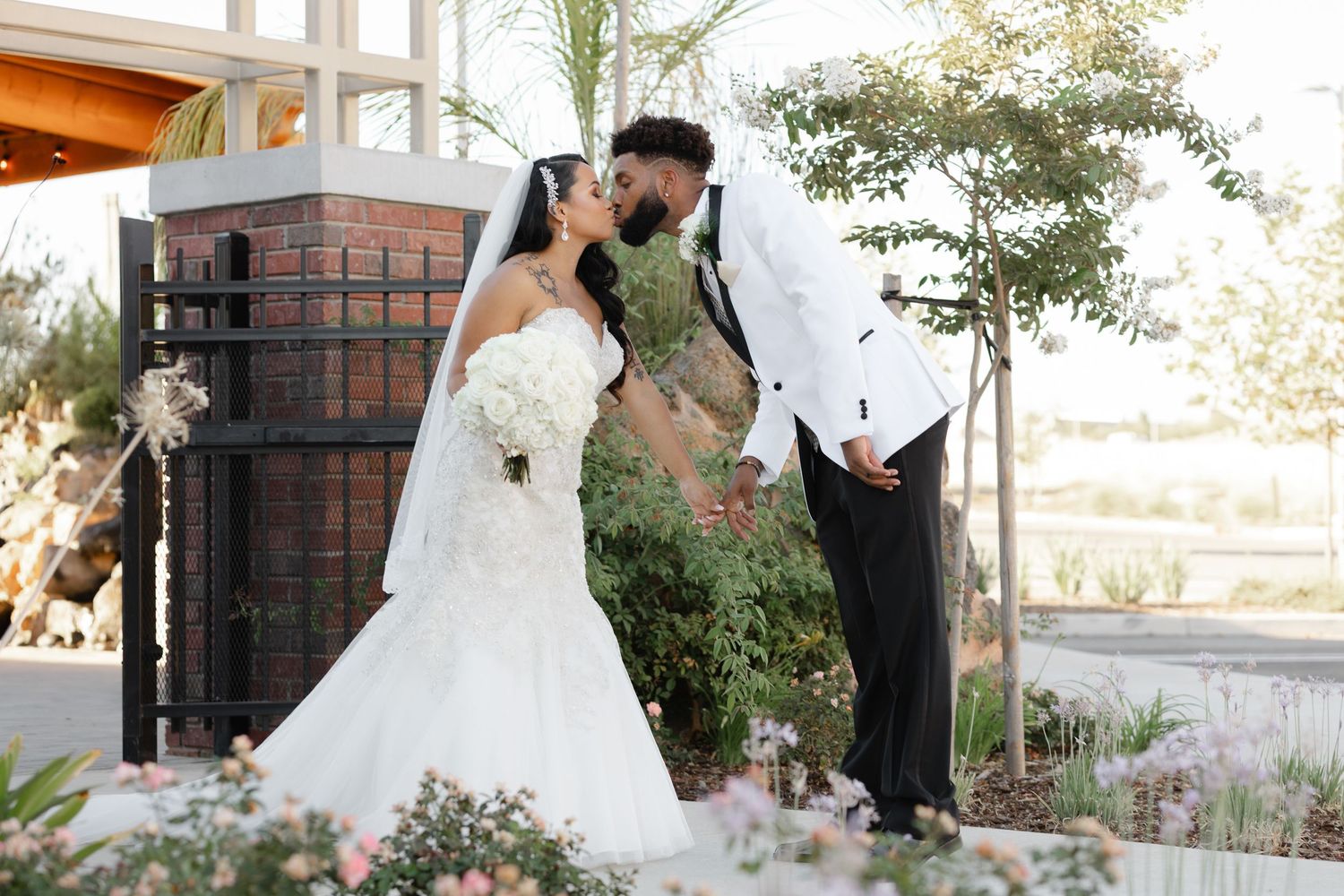 A romantic outdoor wedding moment in front of a rustic wooden door surrounded by lush greenery and flowers.
