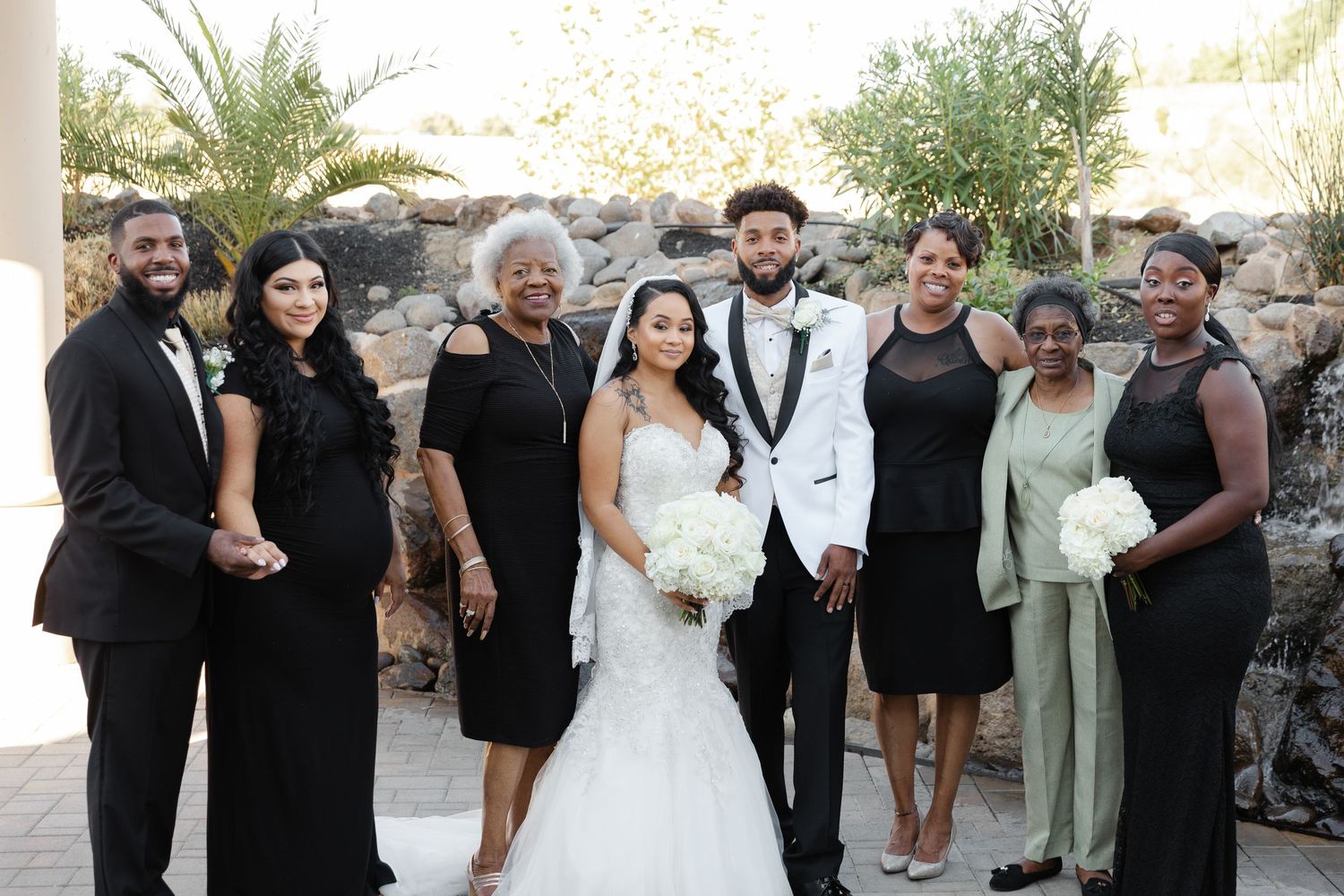 A formal wedding party poses together outdoors wearing elegant black and white attire for a special celebration.