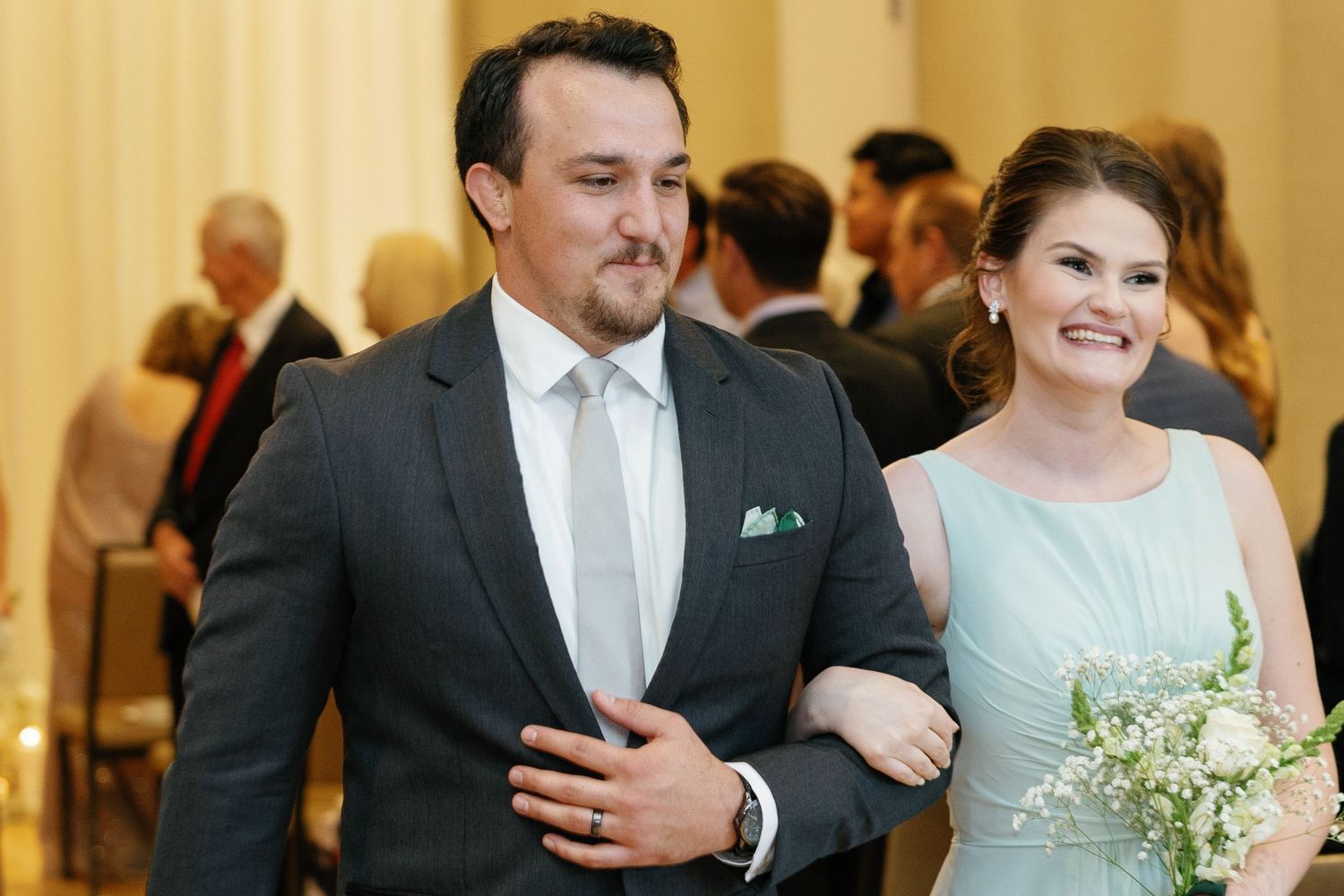 A bride and groom share their first dance surrounded by guests at an elegant indoor wedding reception.