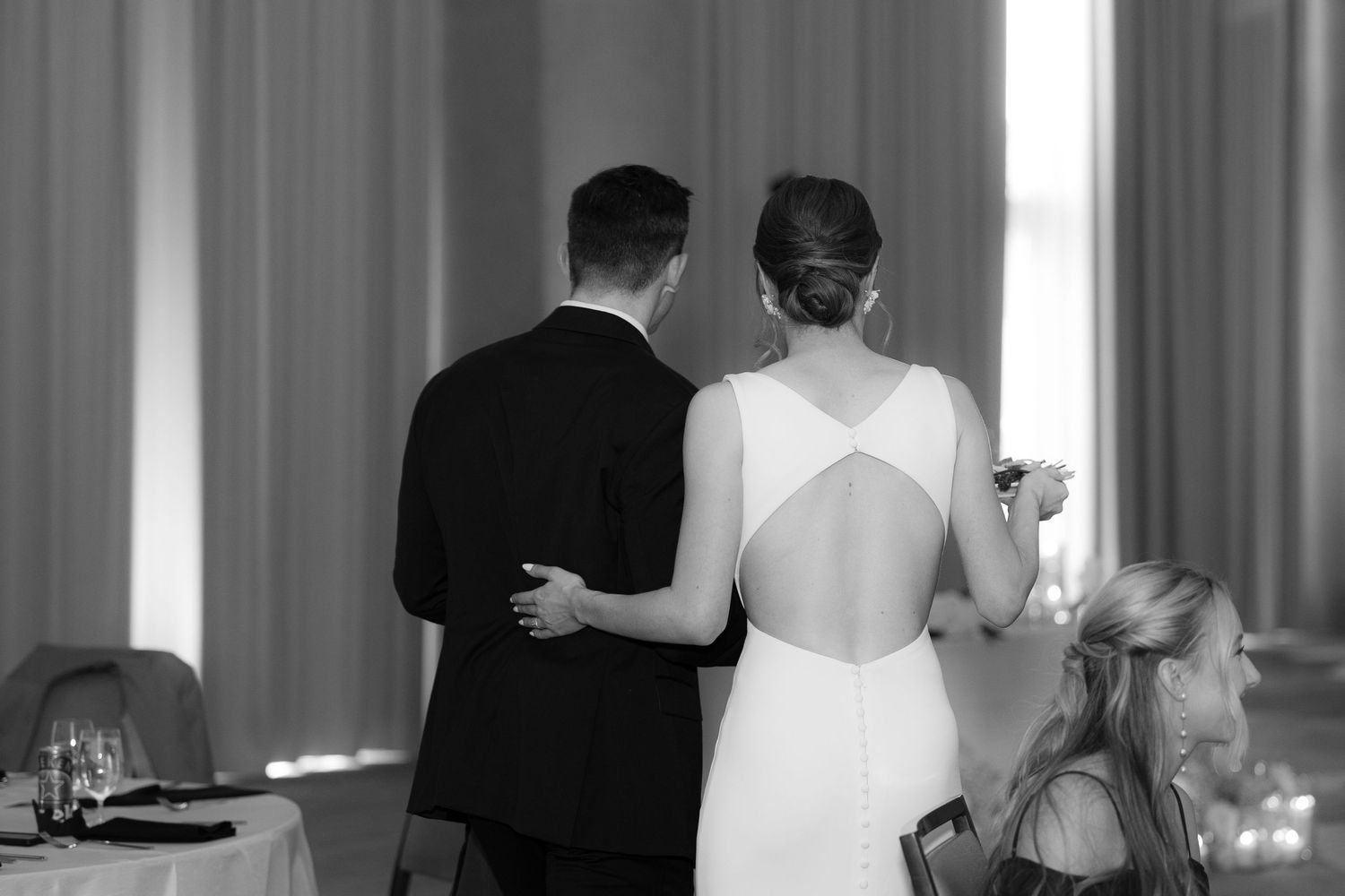Black and white photo of a couple at their wedding reception, with the bride wearing an elegant backless gown.