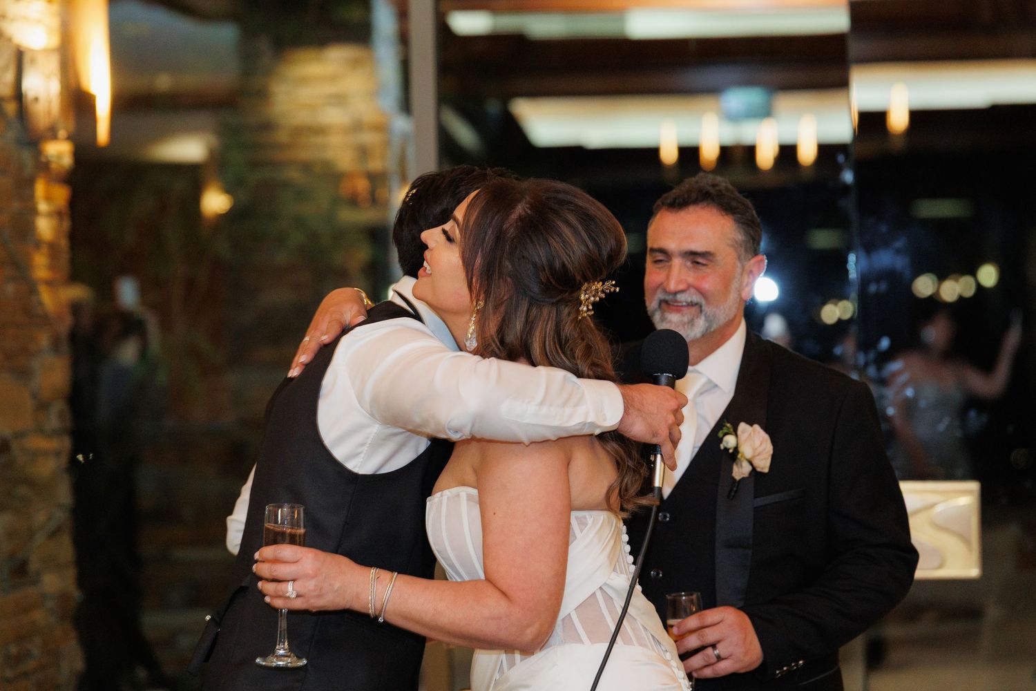 Wedding guests celebrate and dance together during an evening reception in a dimly lit venue.