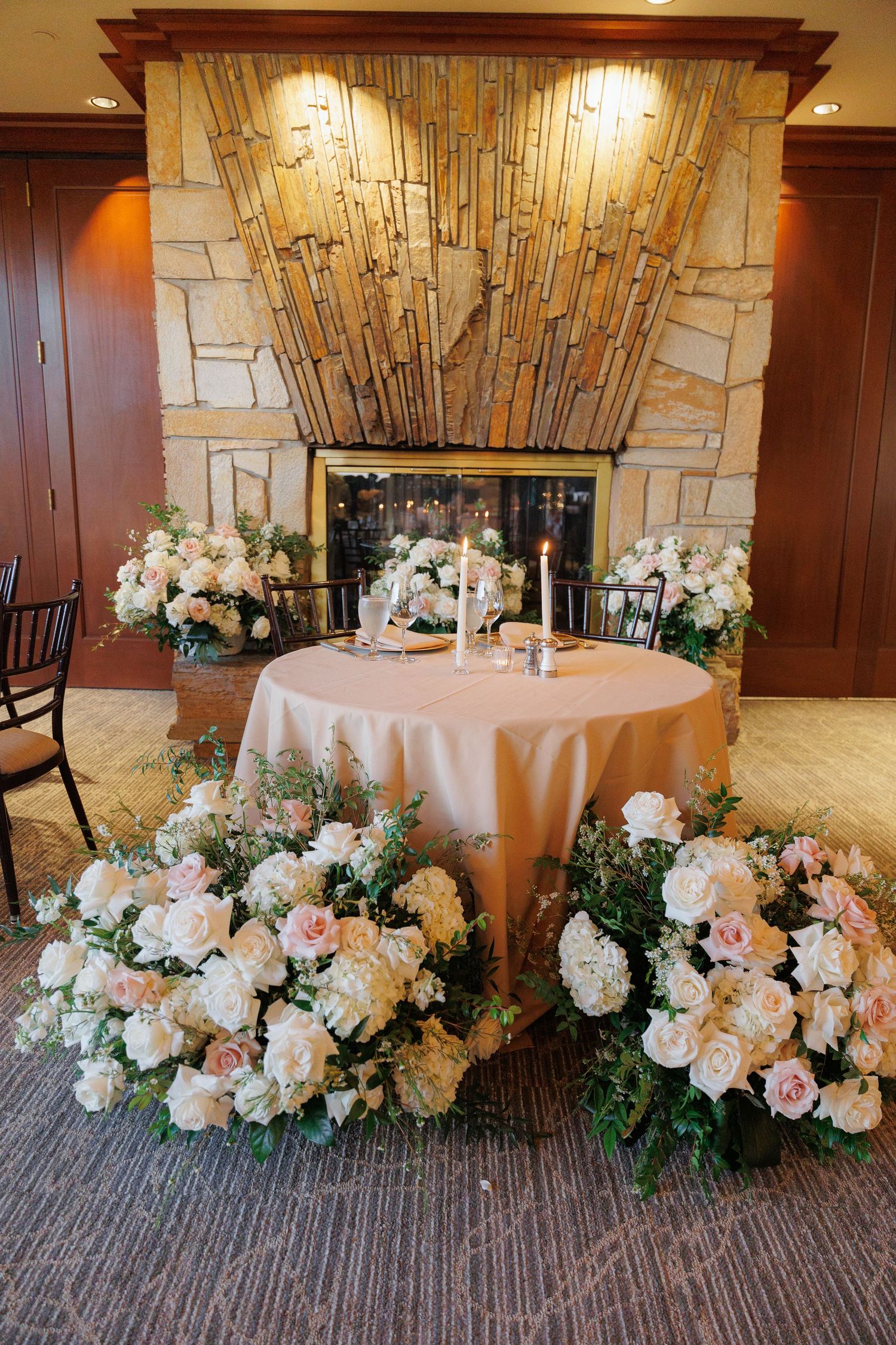 Elegant wedding reception table decor with lush white and peach floral arrangements along the base in an upscale venue.