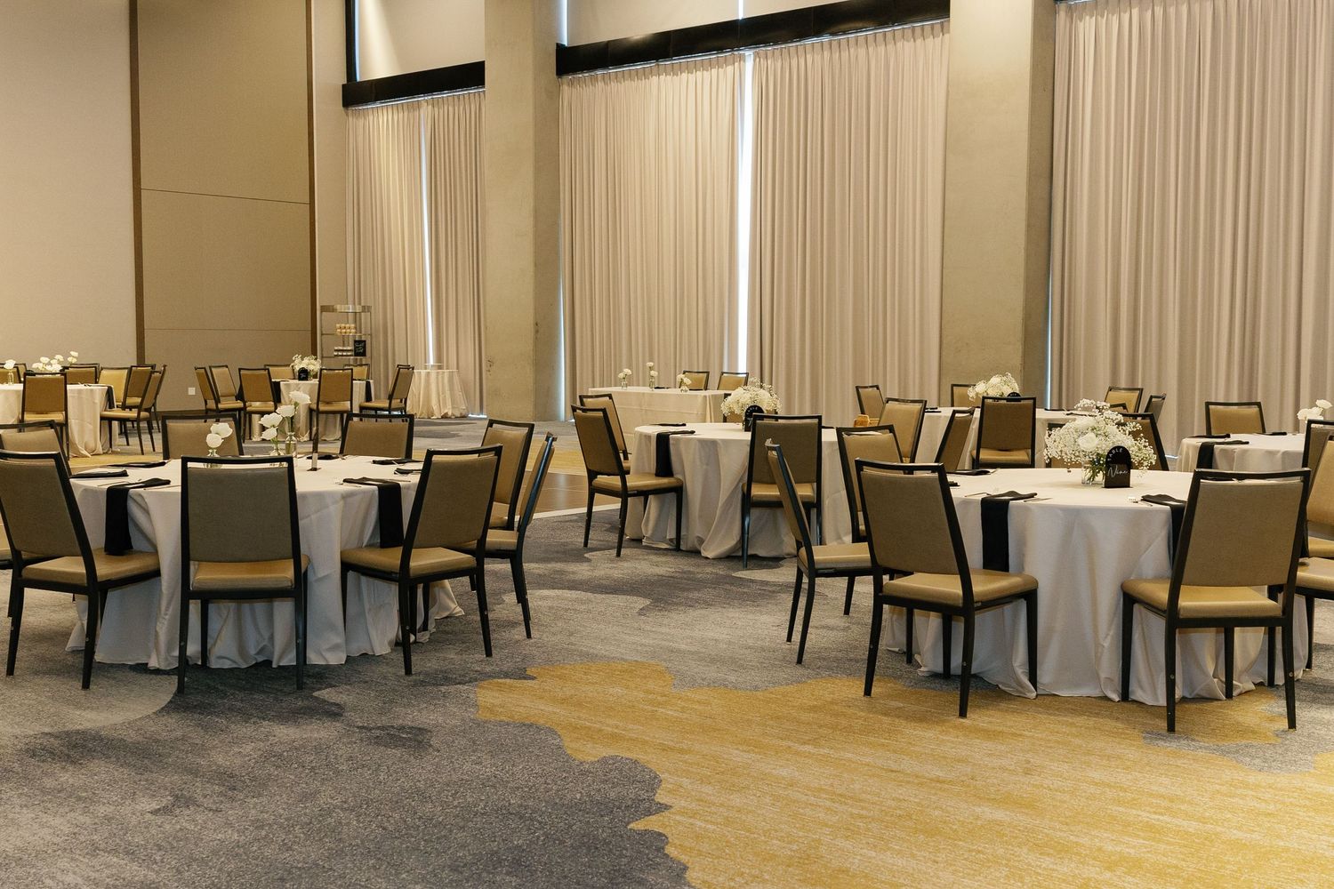An elegant banquet hall with round tables, cream colored chairs and white tablecloths arranged in neat rows.
