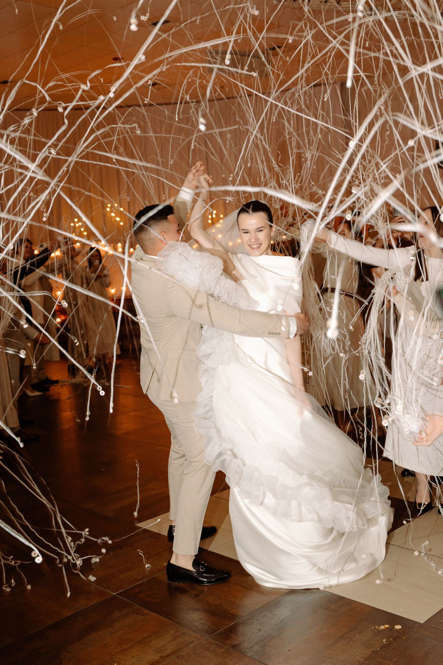 A newlywed couple dances under a shower of white streamers during their wedding reception celebration.
