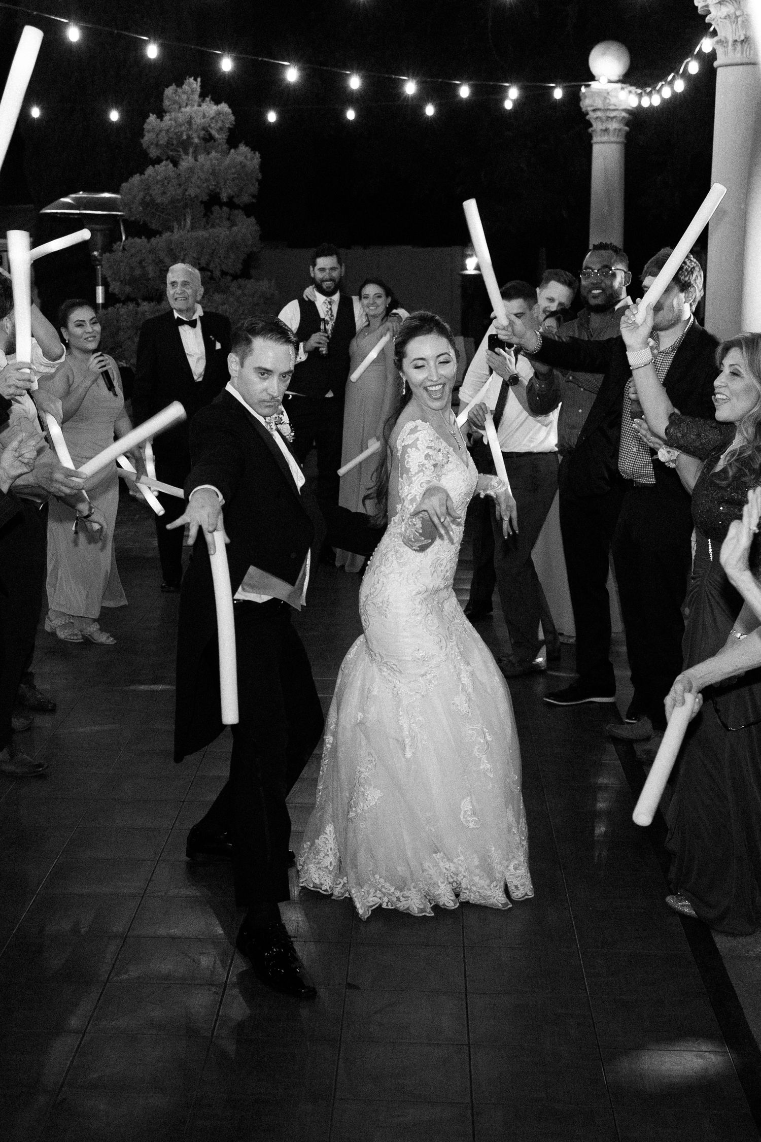 Wedding celebration on a dance floor with guests holding light-up foam sticks under string lights.