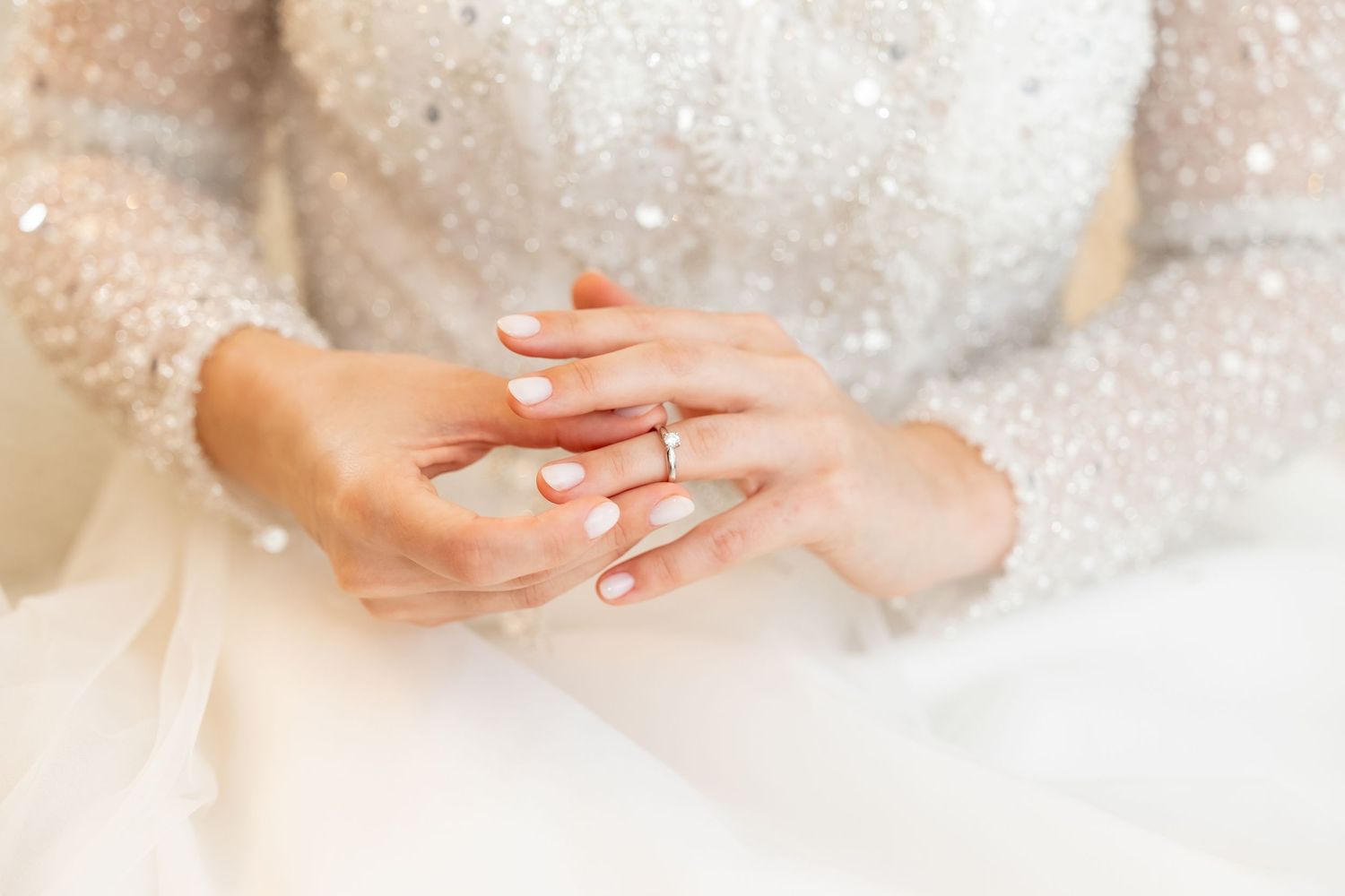 Close-up view of hands gently applying moisturizing cream on soft skin with sparkly glitter effect in background.