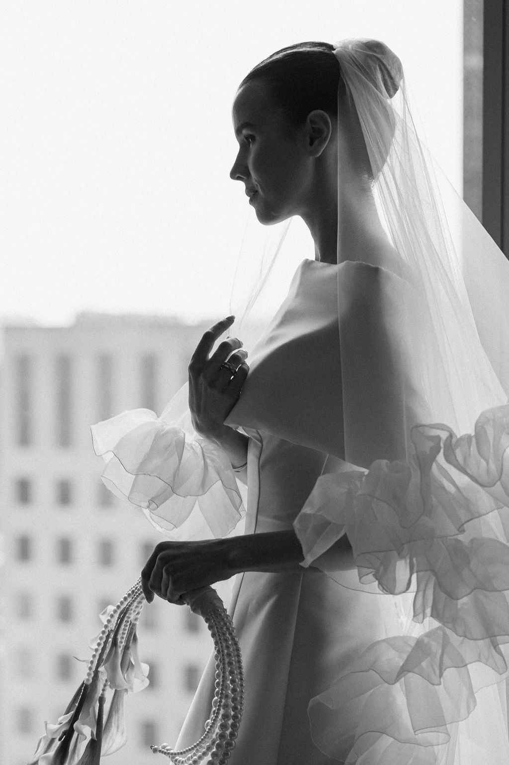 Elegant bridal silhouette in black and white shows a flowing wedding dress and veil against a window backdrop.