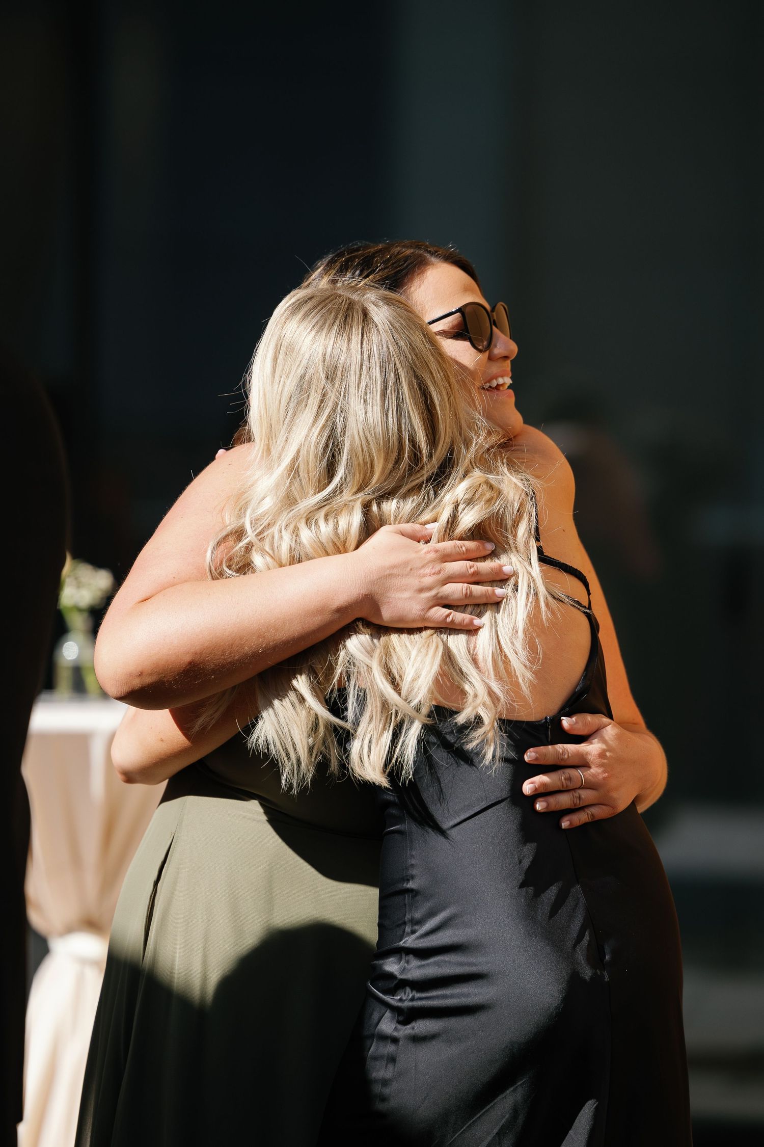 Two women in elegant dresses share a warm embrace at what appears to be a formal event.