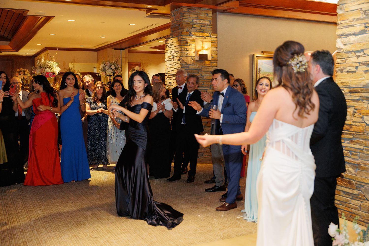 Wedding guests in formal attire gather on a dance floor during an elegant indoor reception celebration.