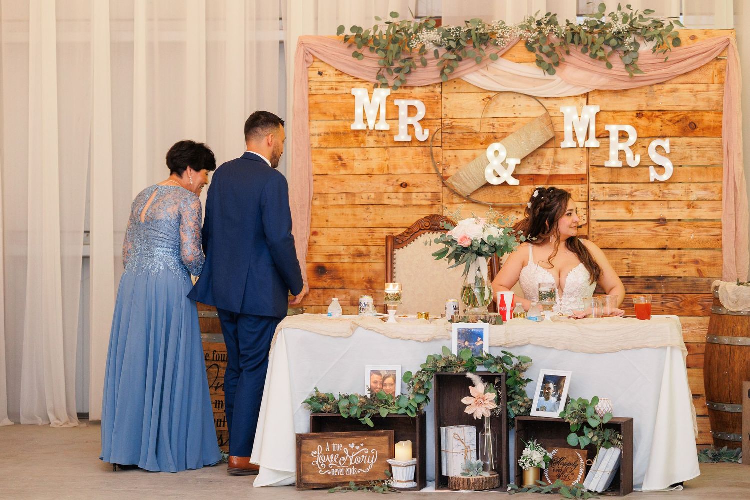 A rustic wedding reception setup with exposed brick walls, white curtains, and floral decorations featuring Mr & Mrs signage.