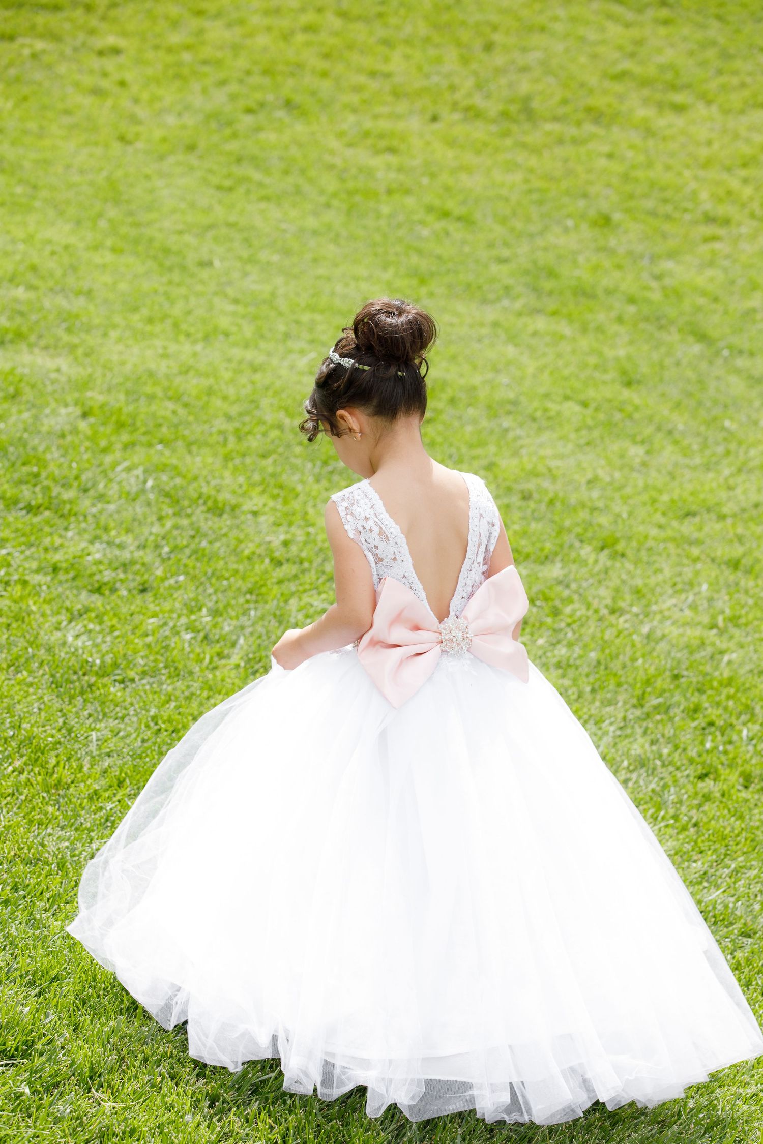 A flowing white tulle flower girl dress twirls gracefully on a bright green lawn in a series of movement shots.