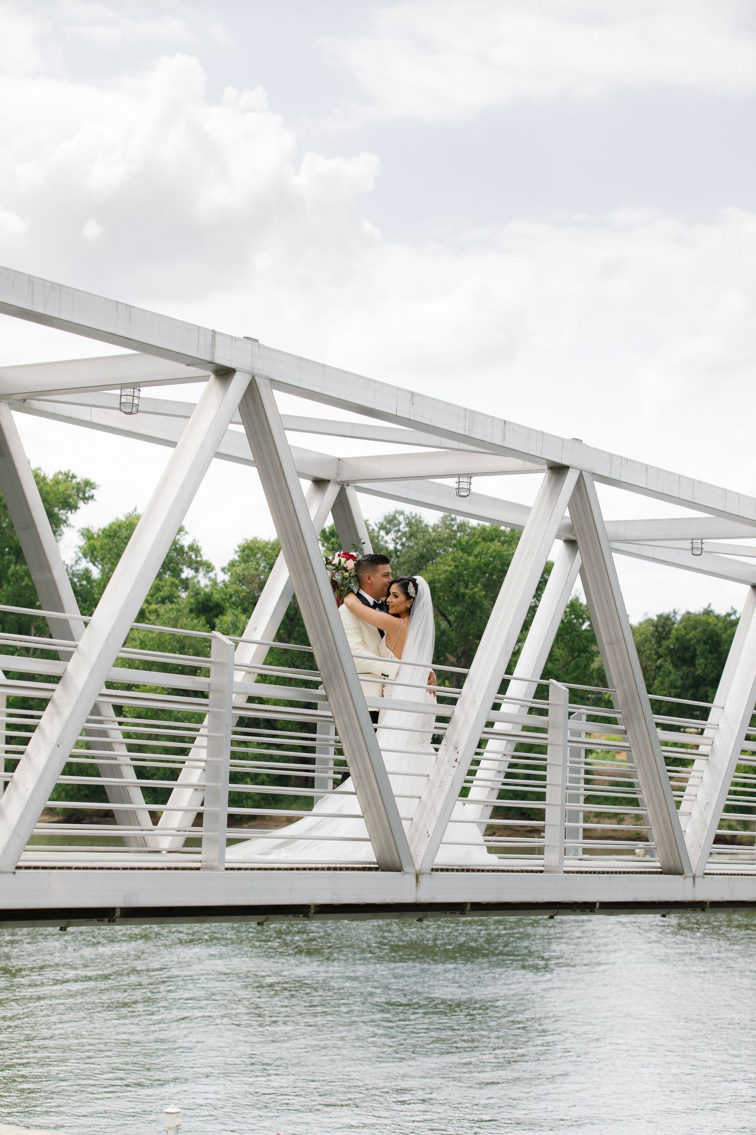A white modern bridge with geometric truss design spans across calm blue waters on a cloudy day.