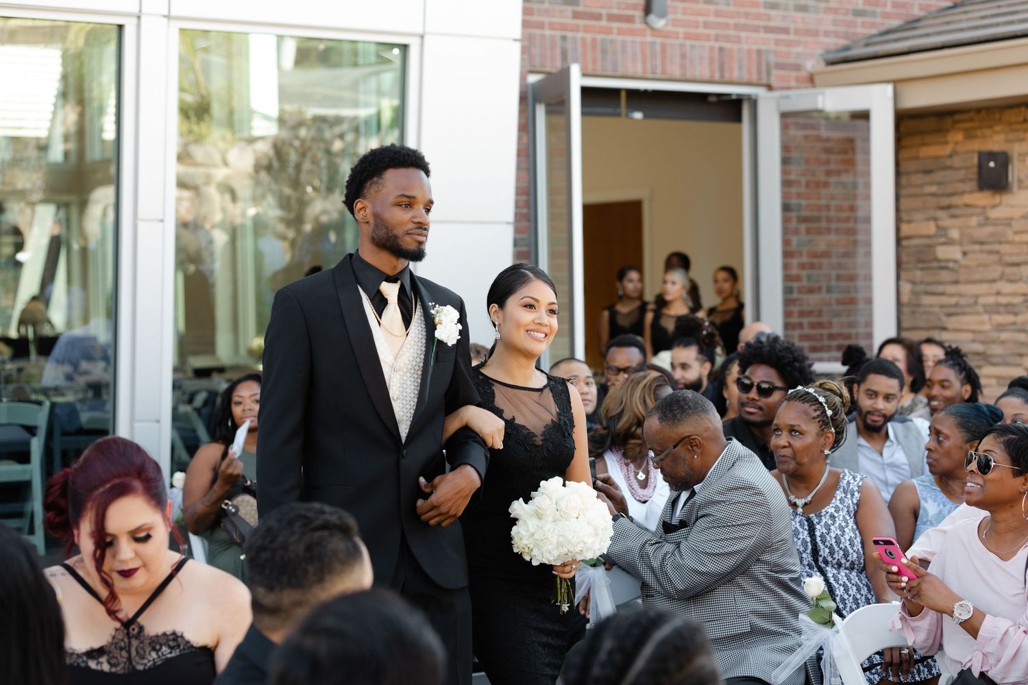 A couple stands together at their outdoor wedding ceremony while guests look on and celebrate the joyous occasion.