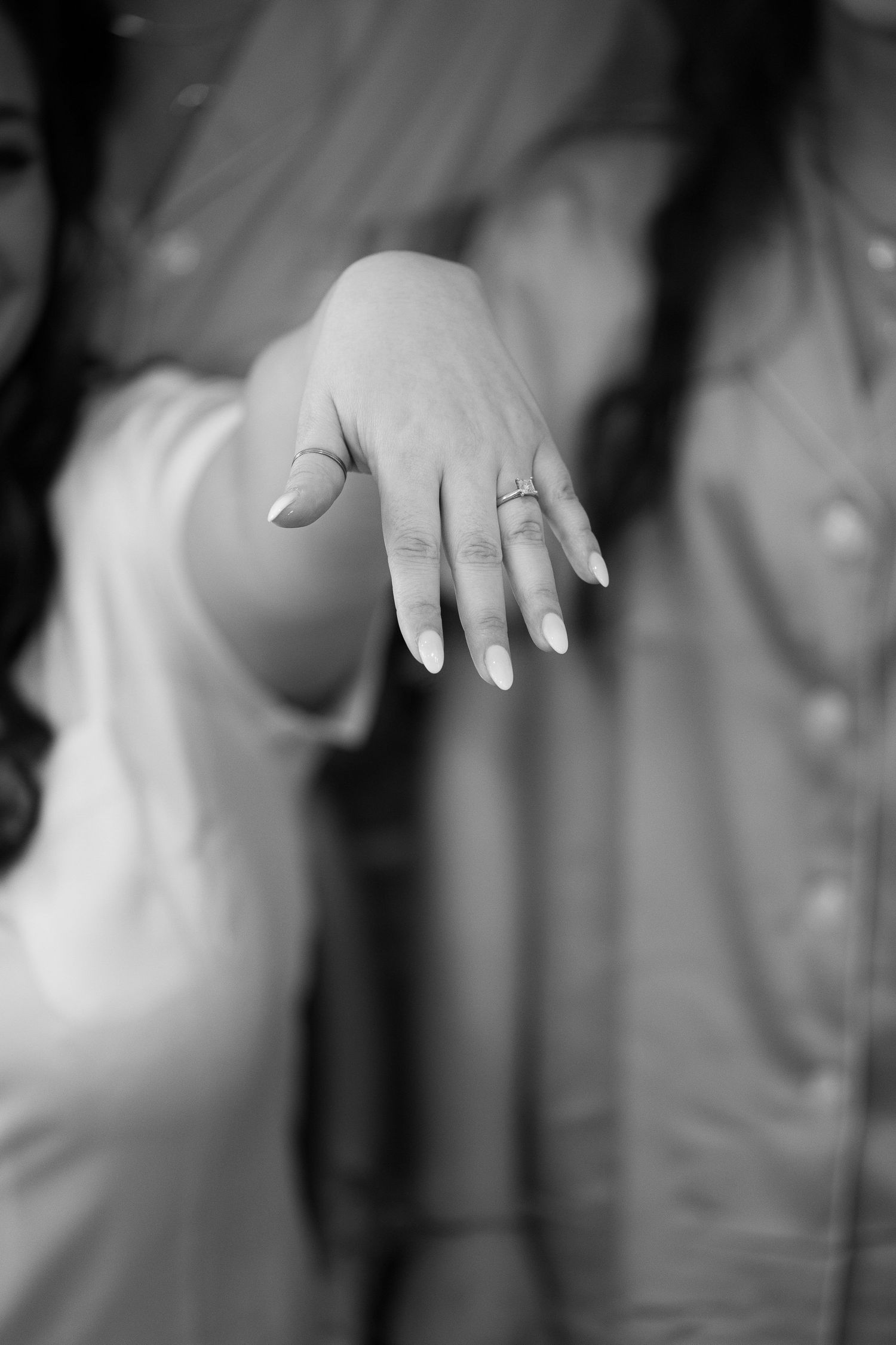 A close-up black and white photo of a hand wearing an engagement ring with manicured nails.