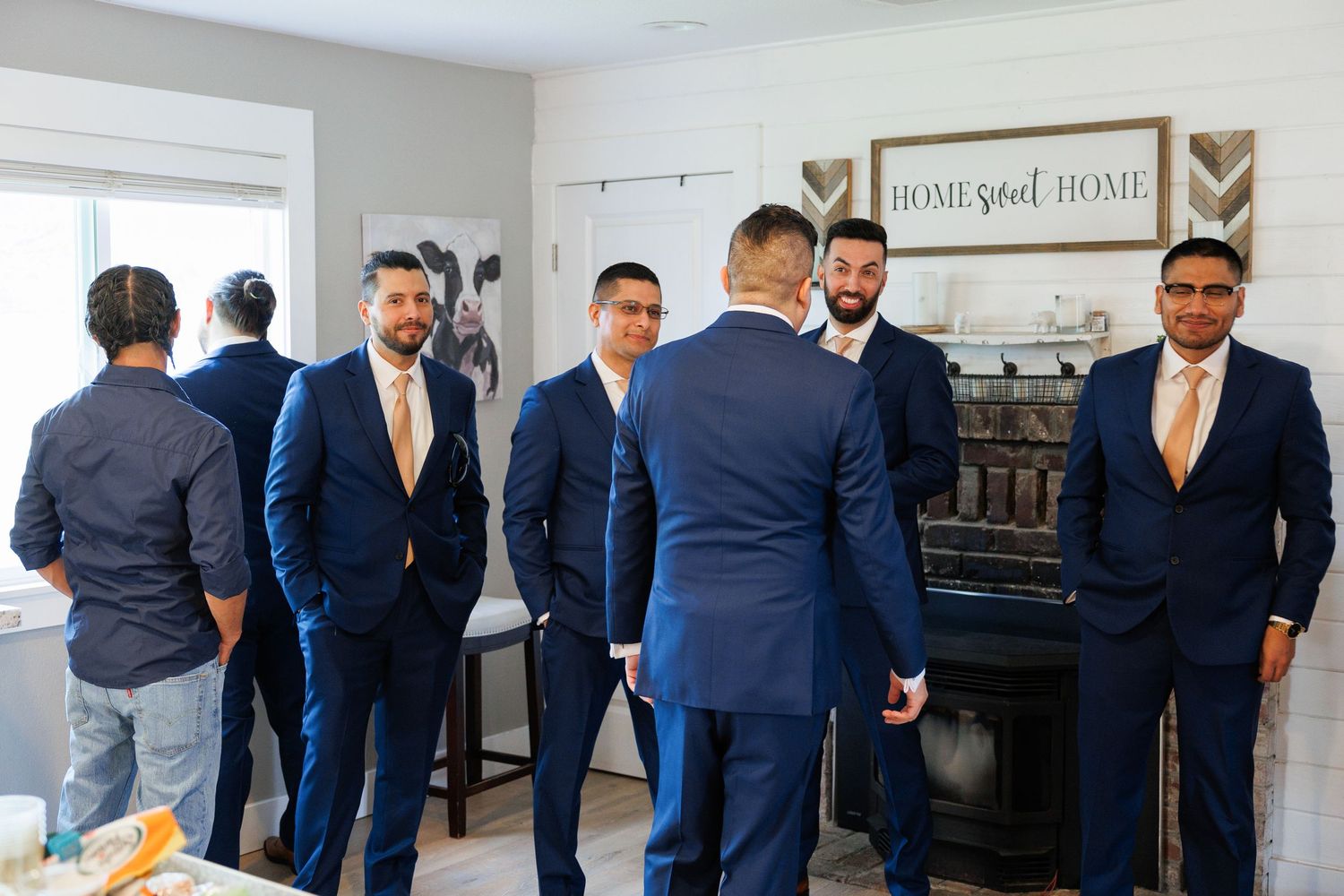 Groomsmen in navy blue suits gather together while getting ready in a bright room with white walls.