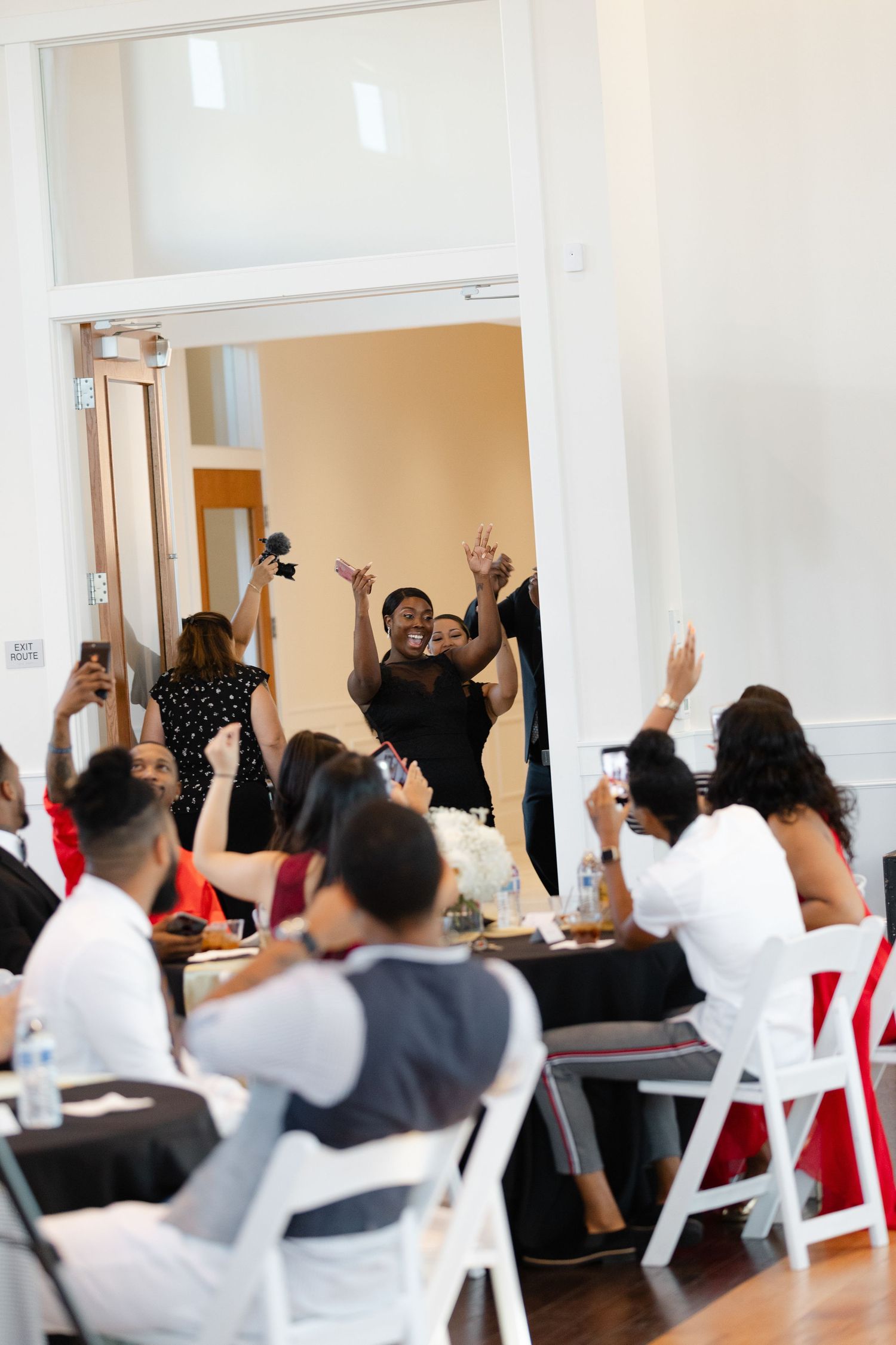 Students raise their hands during an interactive classroom session with white chairs and beige walls.