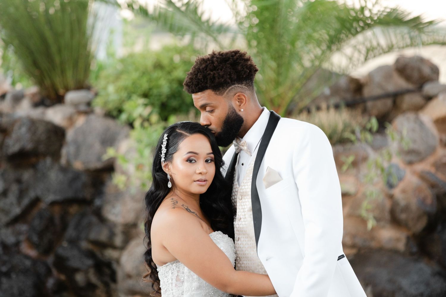 Romantic couple in formal attire embracing during outdoor photo session with stone wall backdrop.