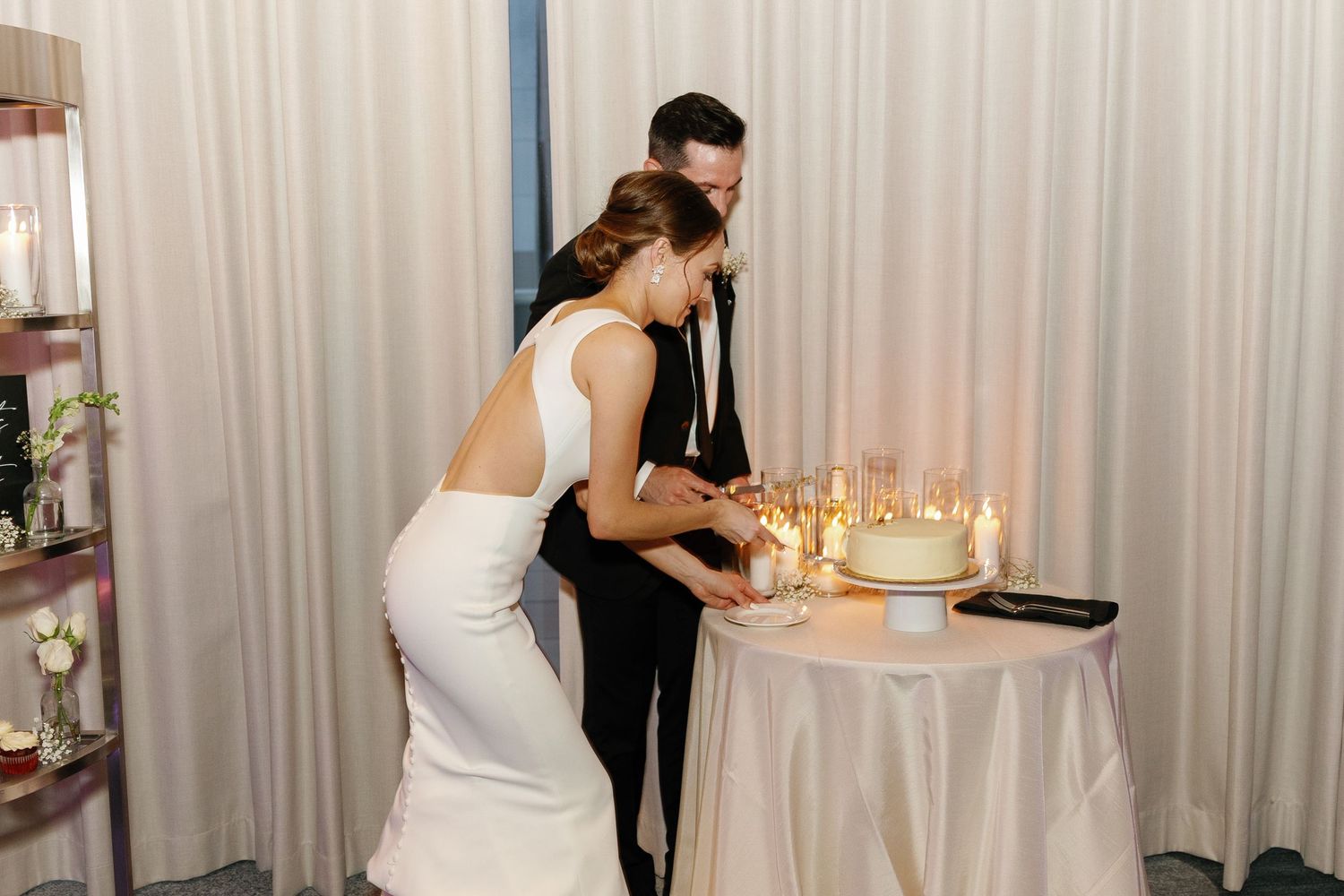 Elegant wedding reception setup with white drapes and small round cocktail tables decorated with candles.