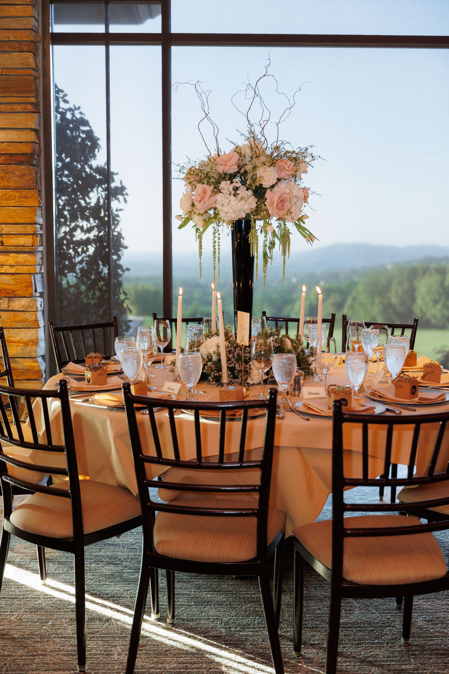 Elegant wedding reception tables with peach linens, floral centerpieces and mountain views through large windows.