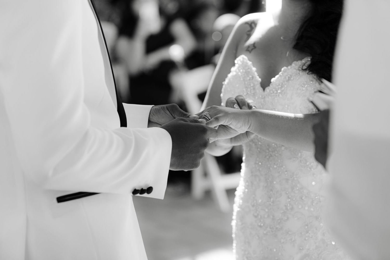 A black and white photo shows a couple in wedding attire sharing a tender moment during their ceremony.