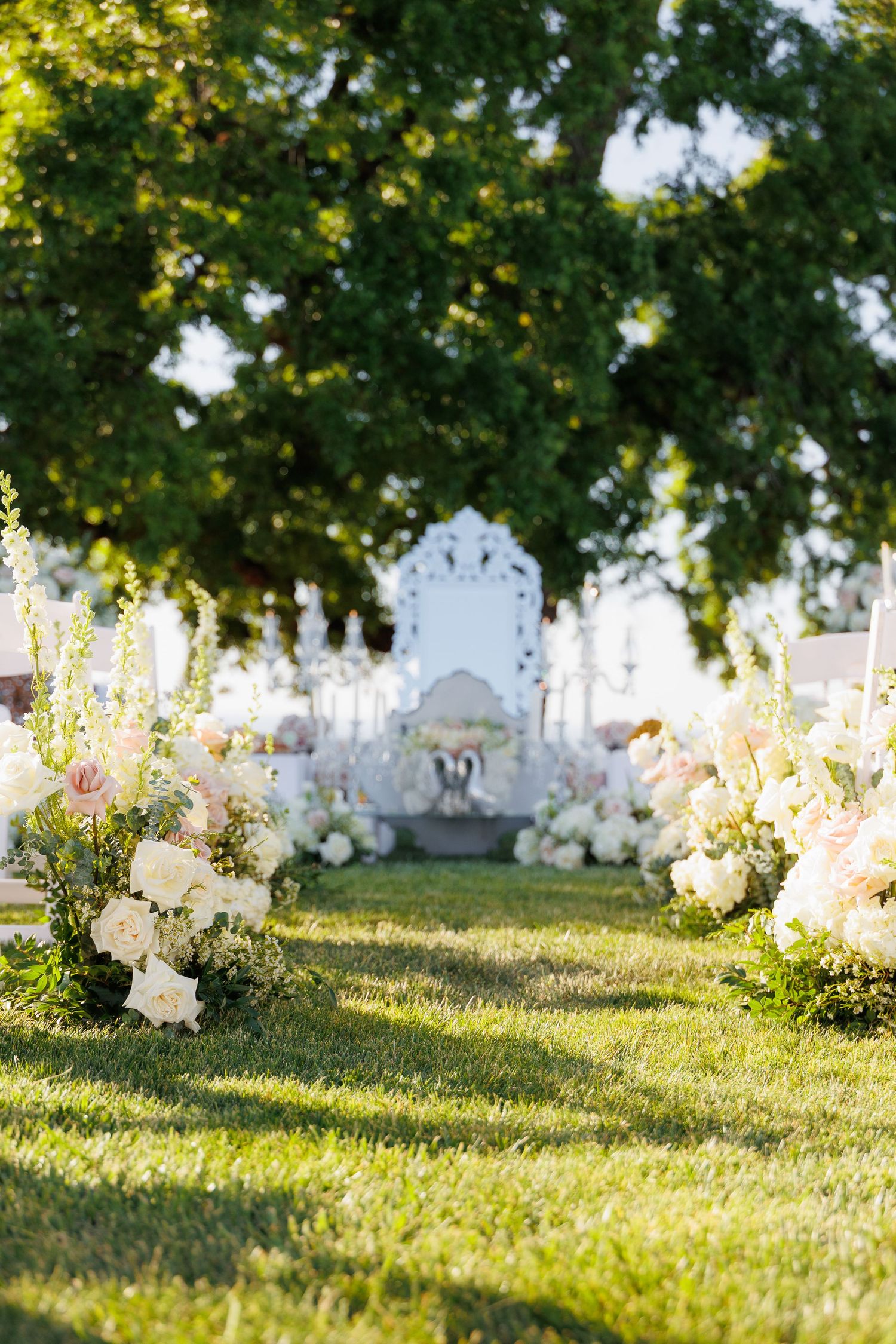 White flowers bloom along a grassy hillside in a cemetery with headstones visible in the background during golden hour.