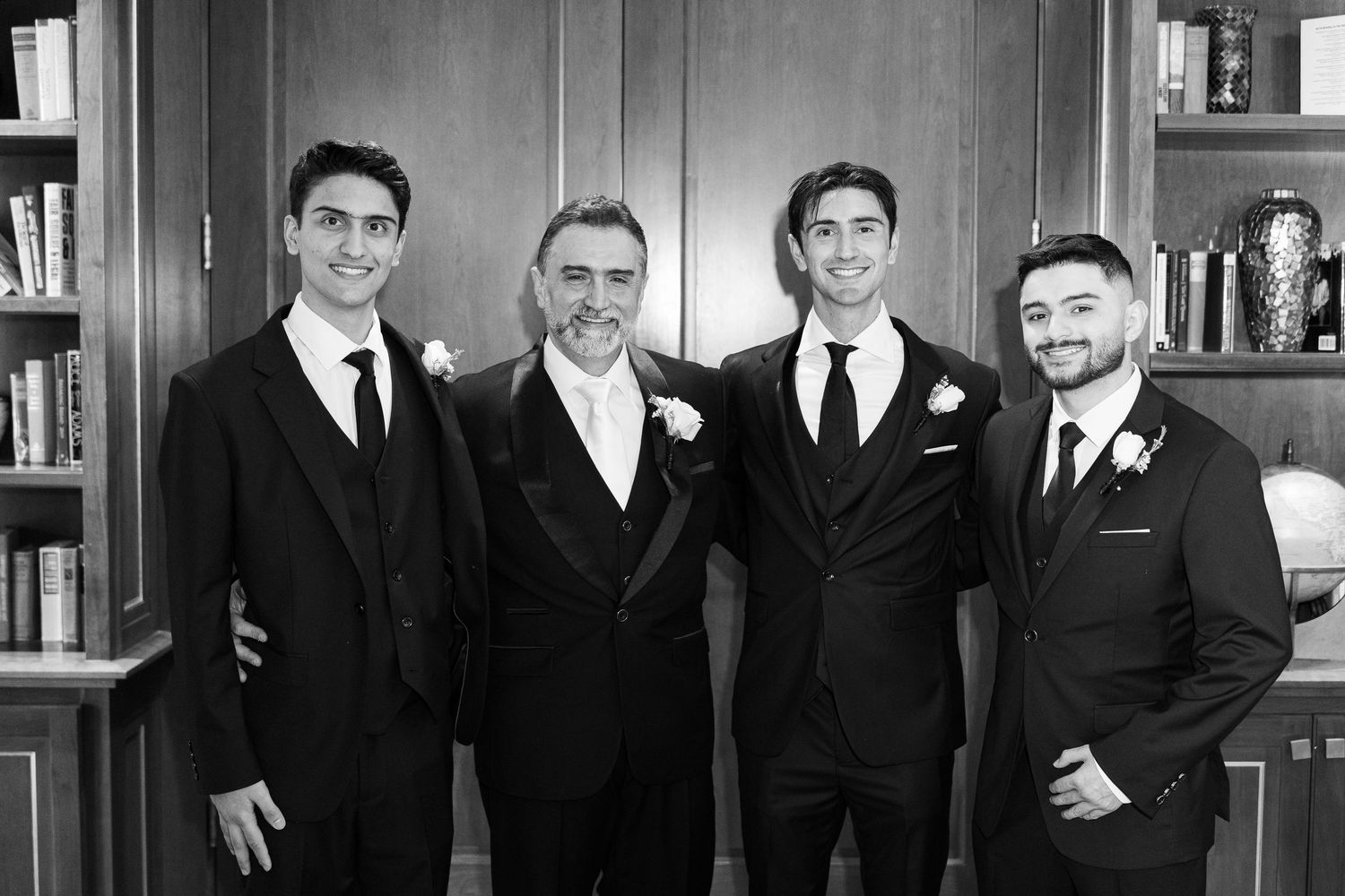A group of formally dressed people in black suits and ties pose together in a black and white photograph.