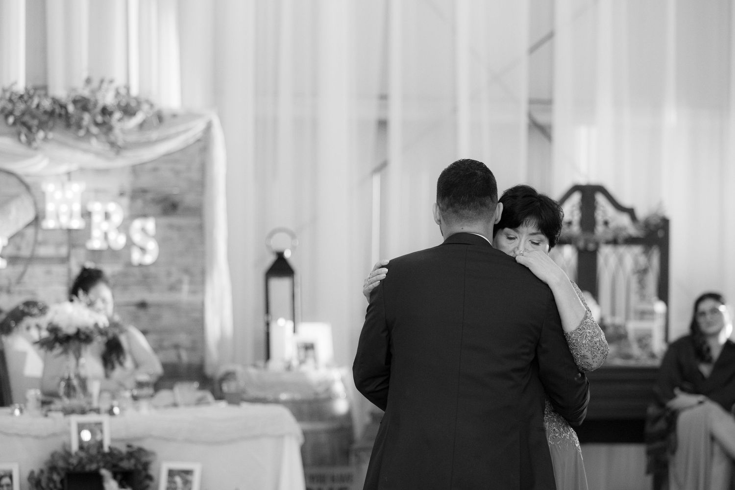 A black and white photo of a couple dancing at a wedding reception with decorative lanterns and signage in the background.