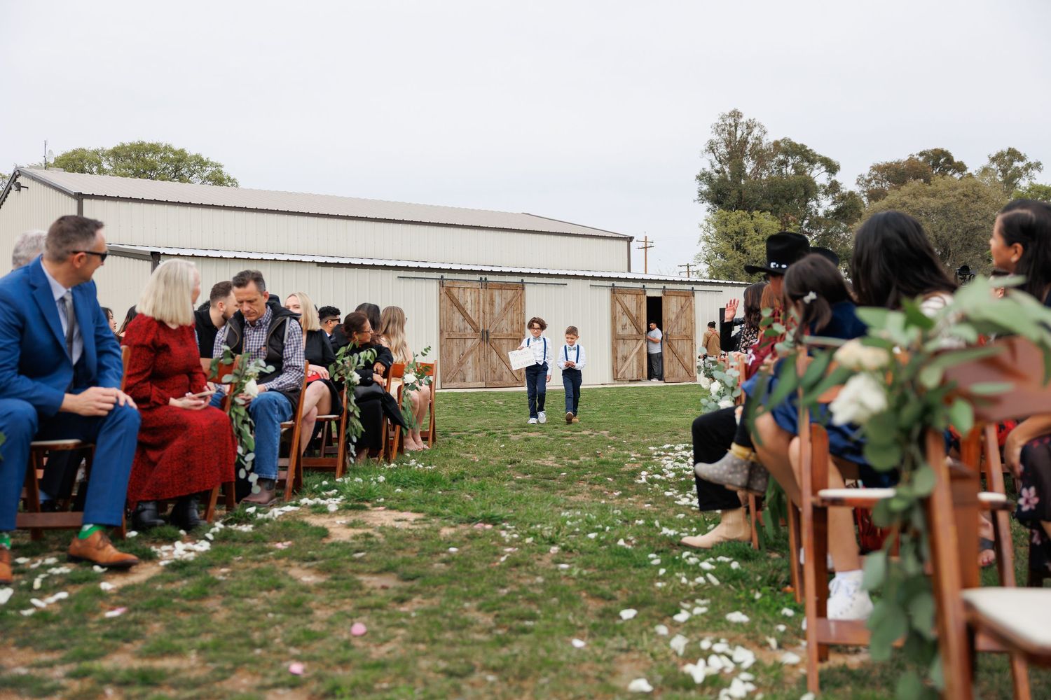 People gather outdoors in a grassy field with buildings visible in the background during a social event.