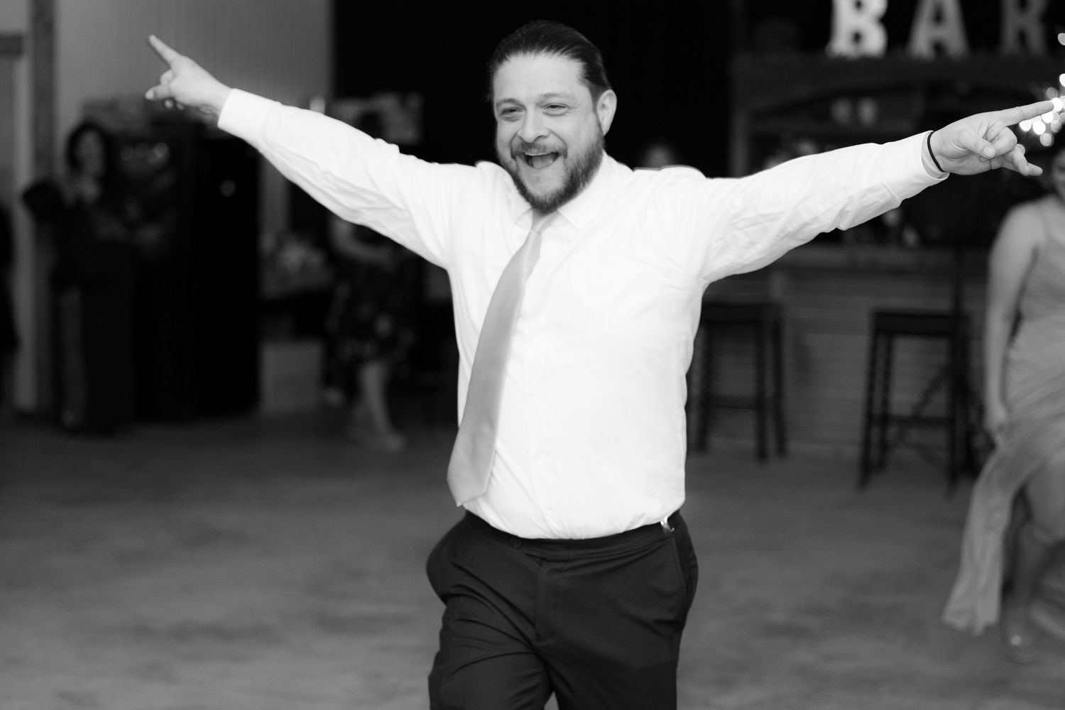 A person in a white shirt spreads their arms wide while standing outdoors in a joyful celebratory pose.