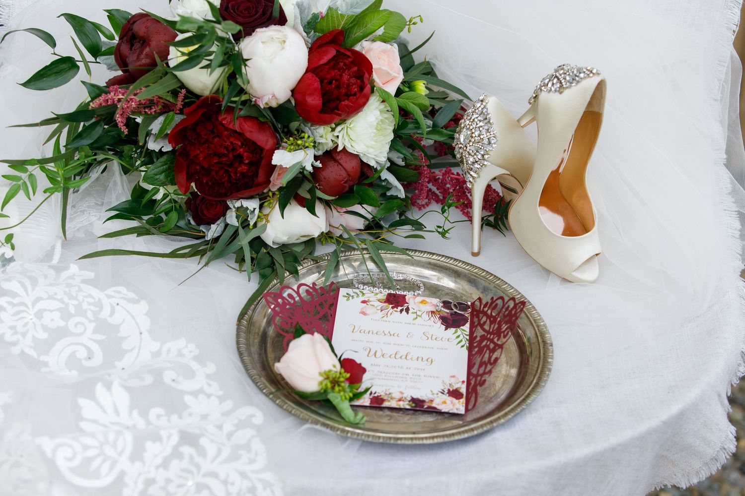 Red roses and white flowers arranged with greenery on elegant silver plates against a white tablecloth.