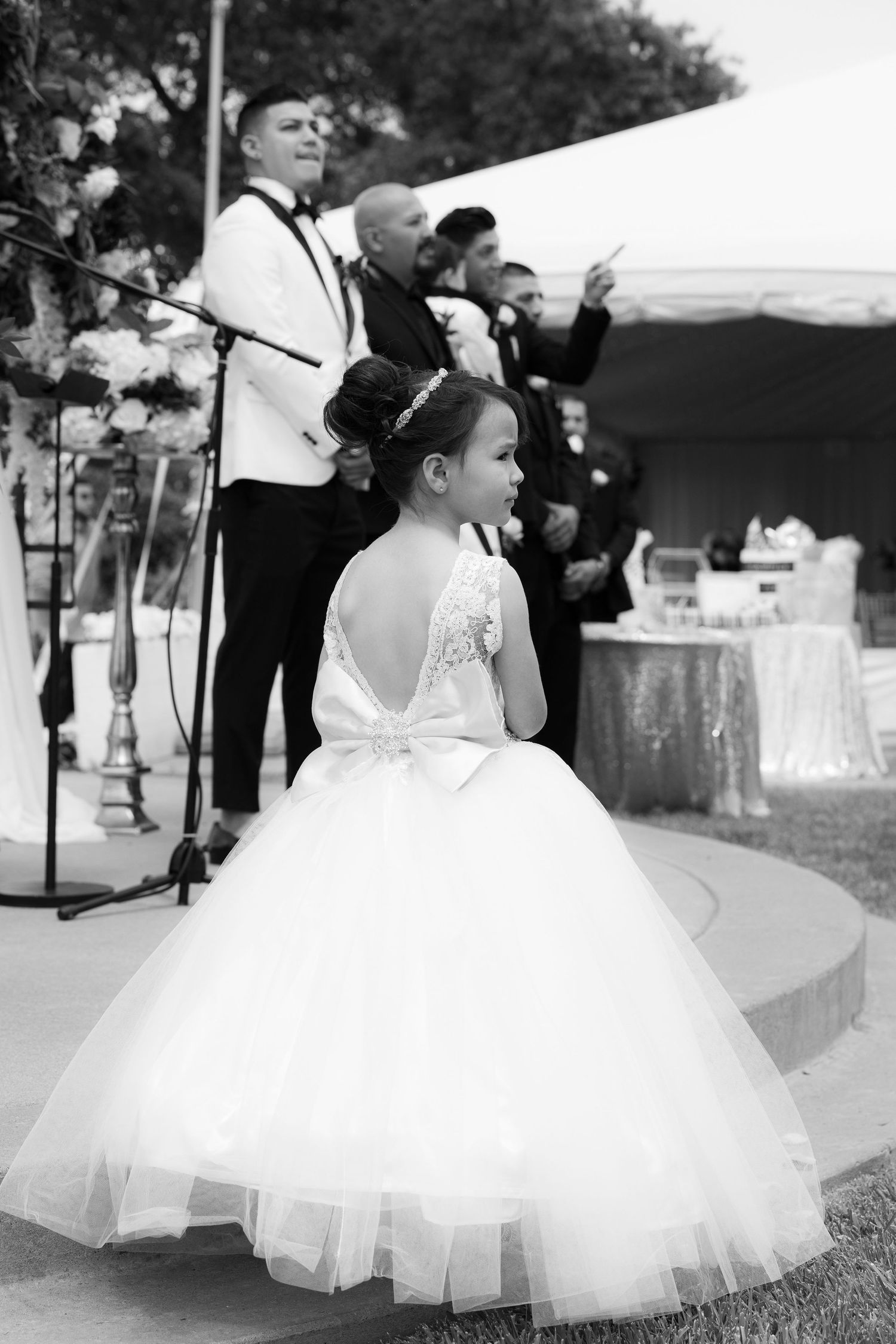 A bride in a voluminous white tulle ball gown twirls gracefully on a grassy lawn during an outdoor wedding reception.