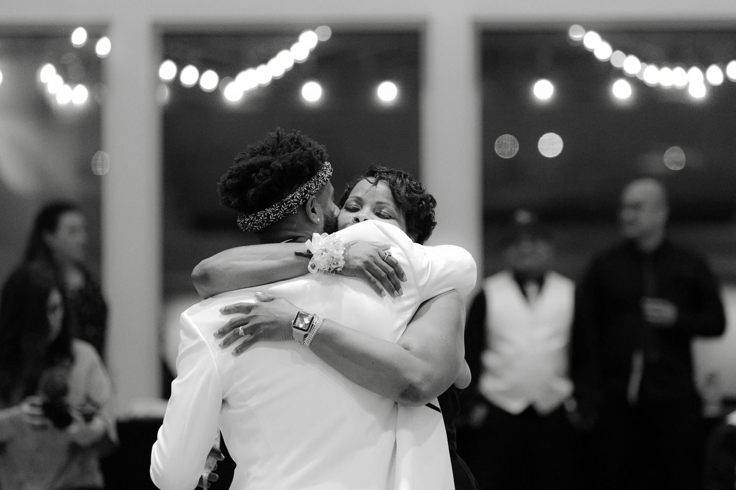 A black and white photograph of a tender dance embrace at an indoor event with twinkling lights in the background.