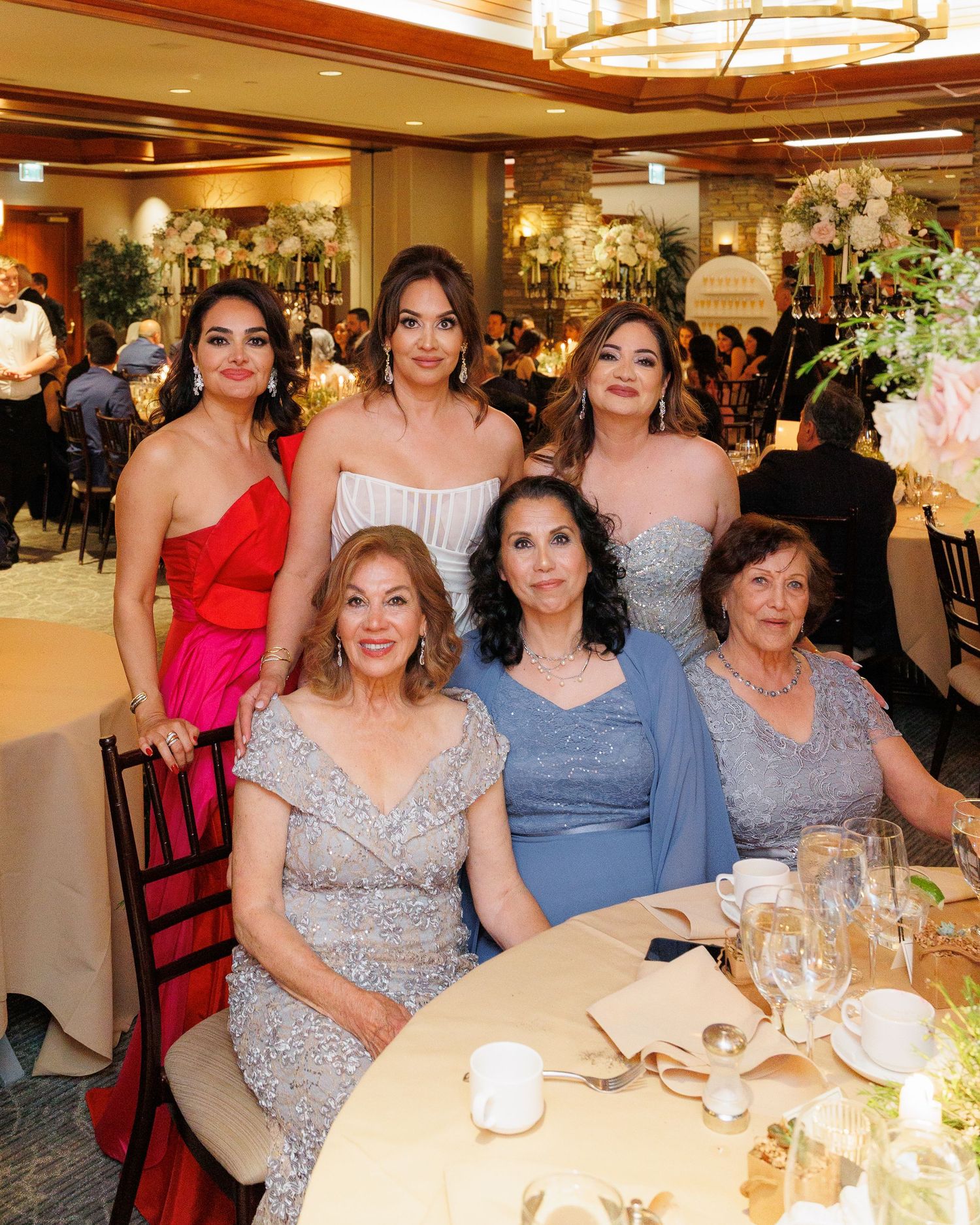 A group of elegantly dressed guests enjoying a formal dinner event at round tables with floral centerpieces.