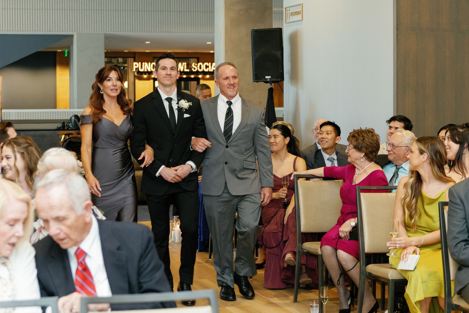 A panoramic view of people gathered in a formal event space with tables and chairs arranged for a celebration.