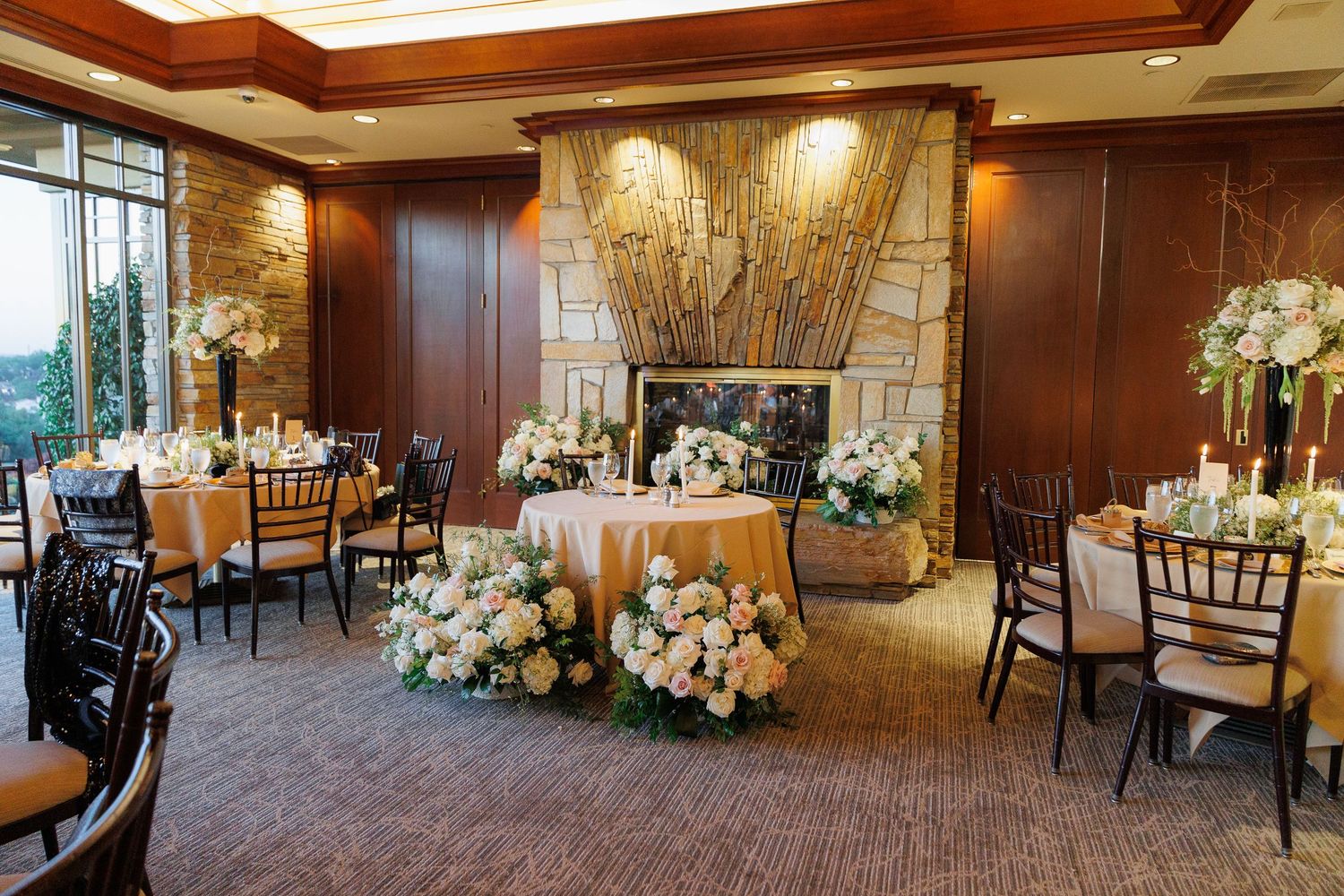 Elegant wedding reception setup with dark wood paneling, floral arrangements and chiavari chairs in an upscale venue.