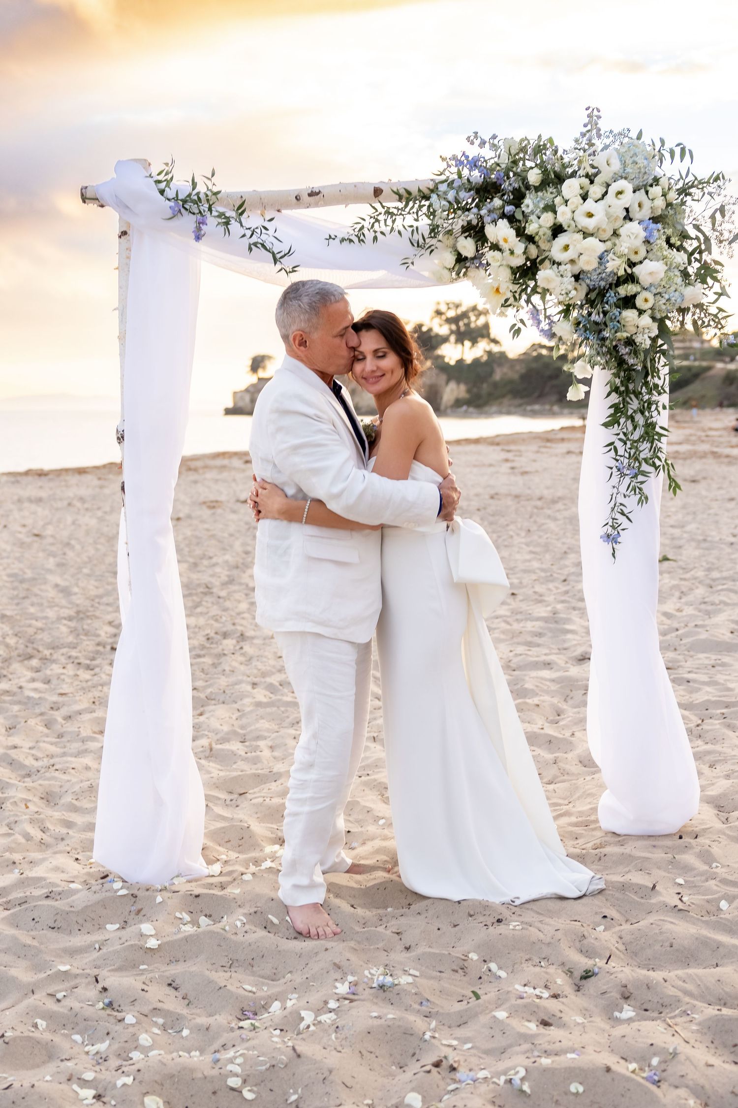 Beach wedding sequence showing couple embracing under white pillars at sunset.