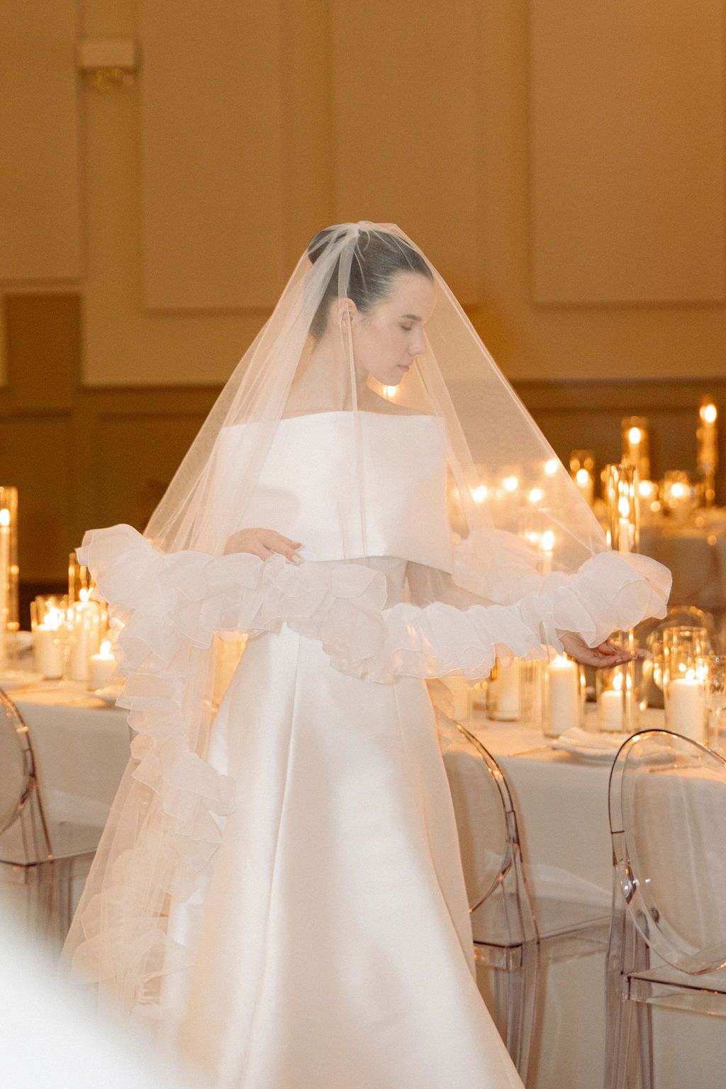 Elegant wedding reception tables set with glowing candles and white decor in a warm-lit ballroom.
